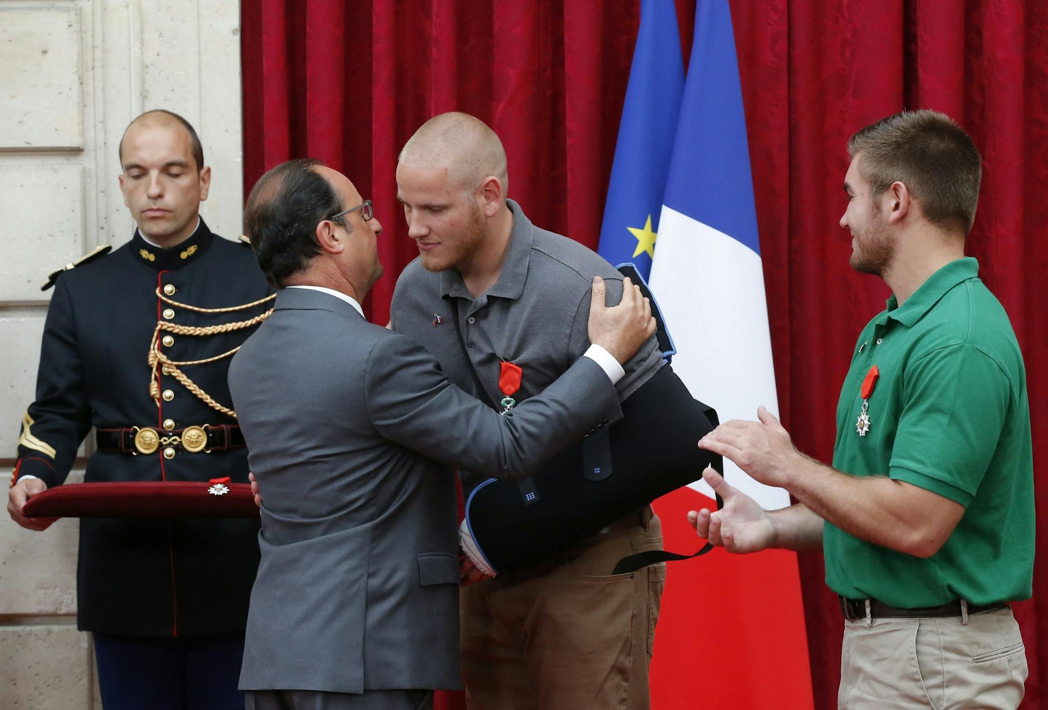 French President Francois Hollande hugs U.S. Airman First Class Spencer Stone, while Oregon National Guard Spc. Alek Skarlatos applauds, after they were awarded a Legion of Honor award with their friend Anthony Sadler, not pictured, at the the Elysee Palace in Paris, Aug. 24, 2015.