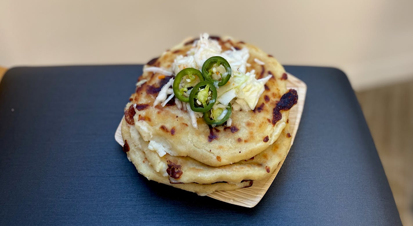 A stack of three griddled pupusas topped with a bit of cabbage slaw and three jalapeno slices.