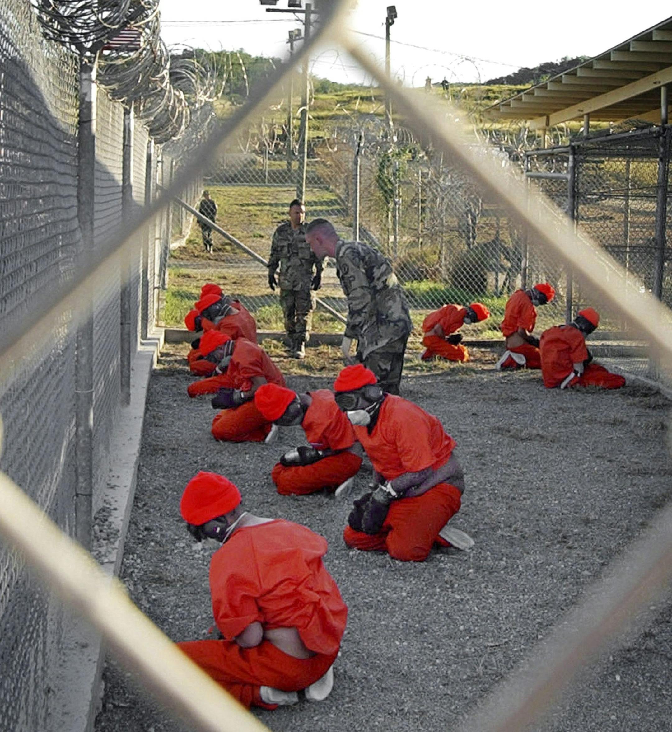 ** FILE ** In this Jan. 11, 2002 file photo, released by the Department of Defense, detainees wearing orange jump suits sit in a holding area as military police patrol during in-processing at the temporary detention facility Camp X-Ray on Guantanamo Bay U.S. Naval Base in Cuba. (AP Photo/U.S. Navy, Shane T.McCoy, File)