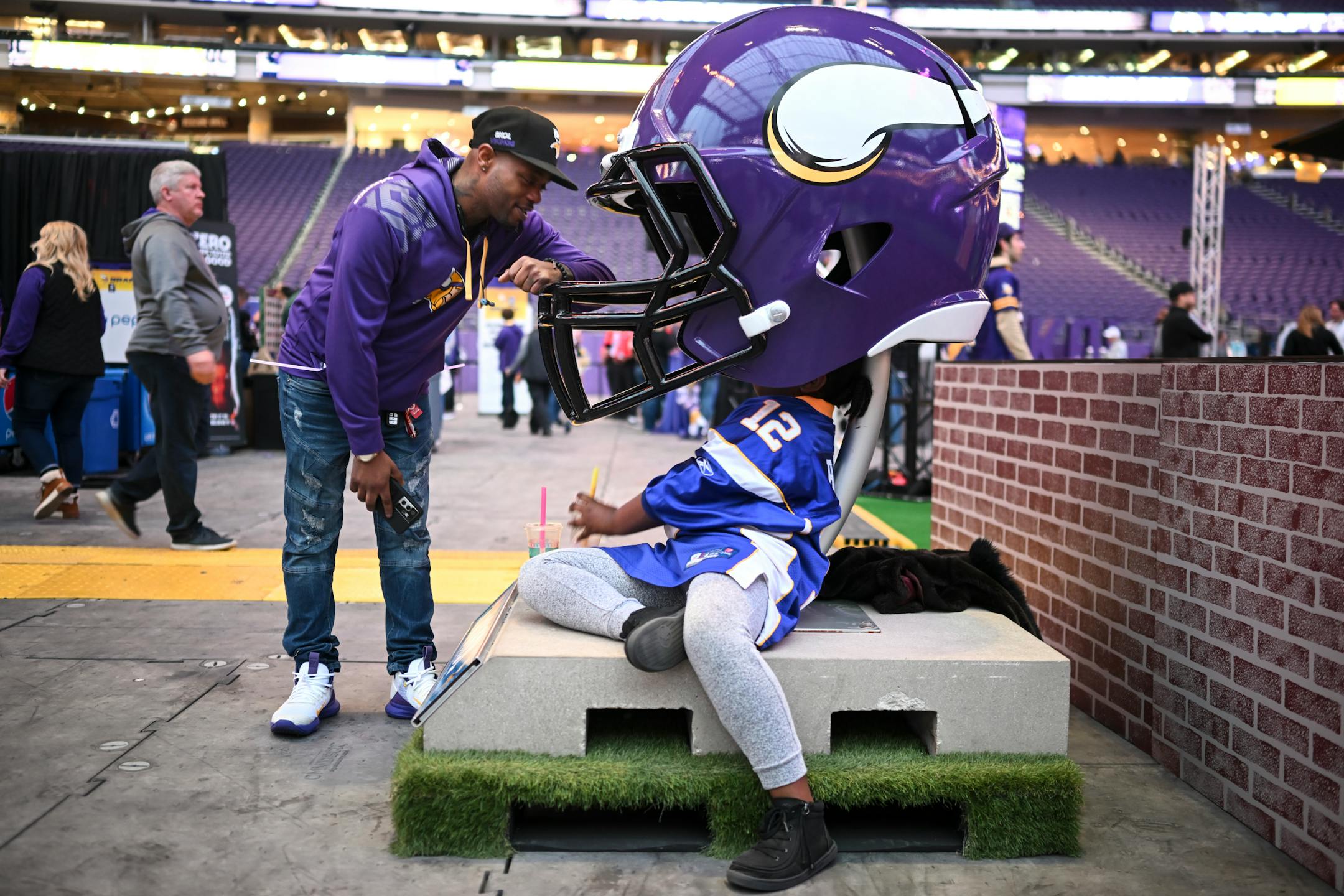 Shaun Allen, of Minneapolis, leans over to talk to his 10-year old daughter, Karma, as she rested under a jumbo Vikings helmet during the Vikings NFL Draft Party.