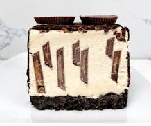 A slice of peanut butter ice cream cake on a plate, with an Oreo cookie crust and peanut butter cups throughout.