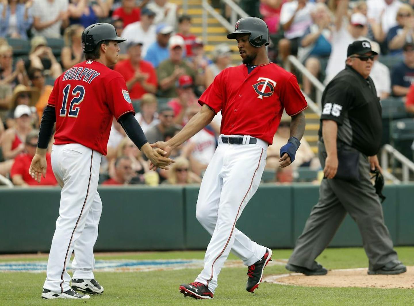 Minnesota Twins' John Ryan Murphy (12) and Byron Buxton, center, congratulate each other after they scored on a Joe Mauer single in the fifth inning of a spring training baseball game against the New York Yankees on Sunday, March 20, 2016, in Fort Myers, Fla. Plate umpire Fieldin Culbreth (25) looks on.