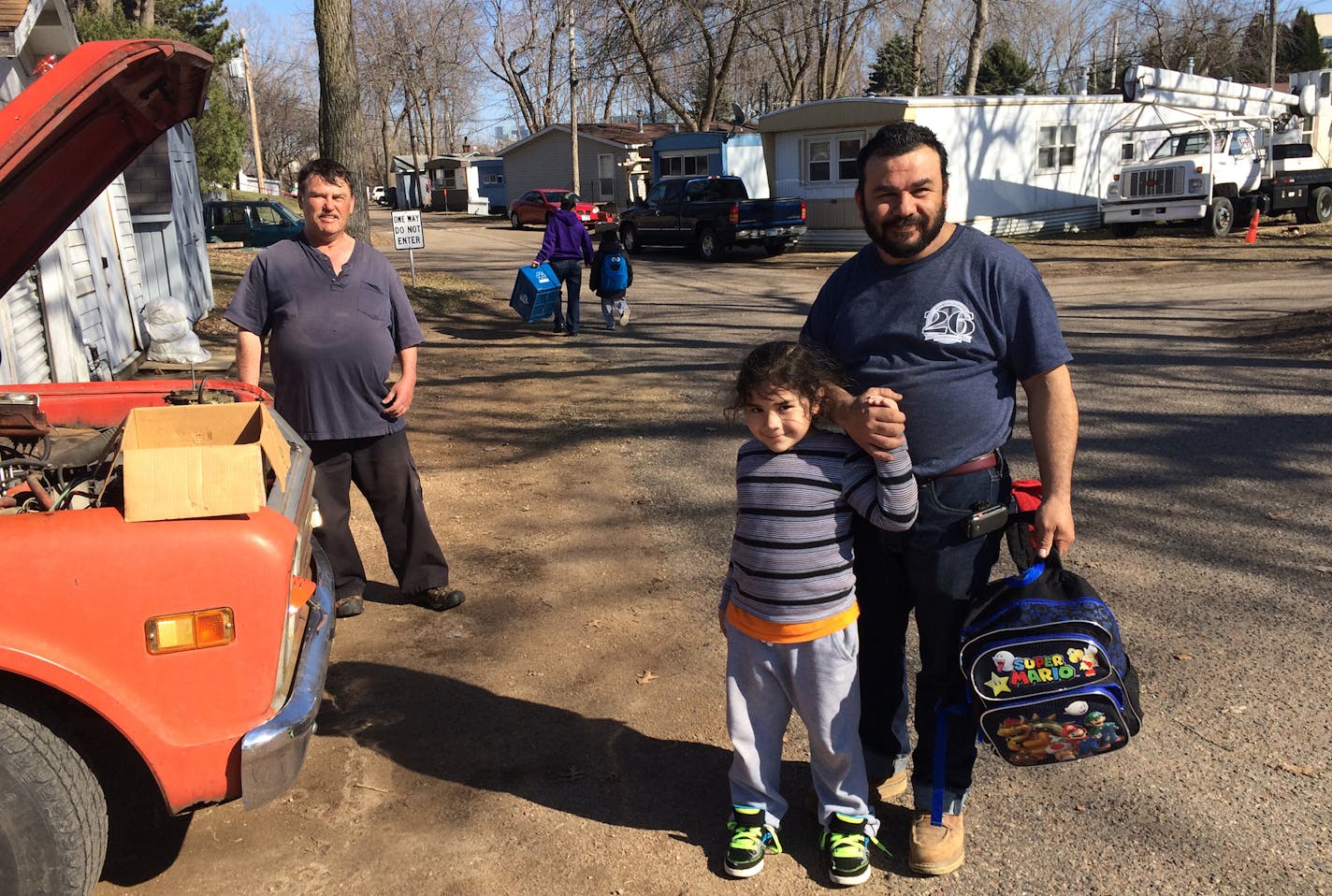 Efrain Gutierrez, right, greeted his son Ezekiel, 6, after getting dropped off by the school bus at Sun Valley mobile home park in Plymouth — neighbor David Witte stood in the background. Gutierrez has lived in Sun Valley for three years.