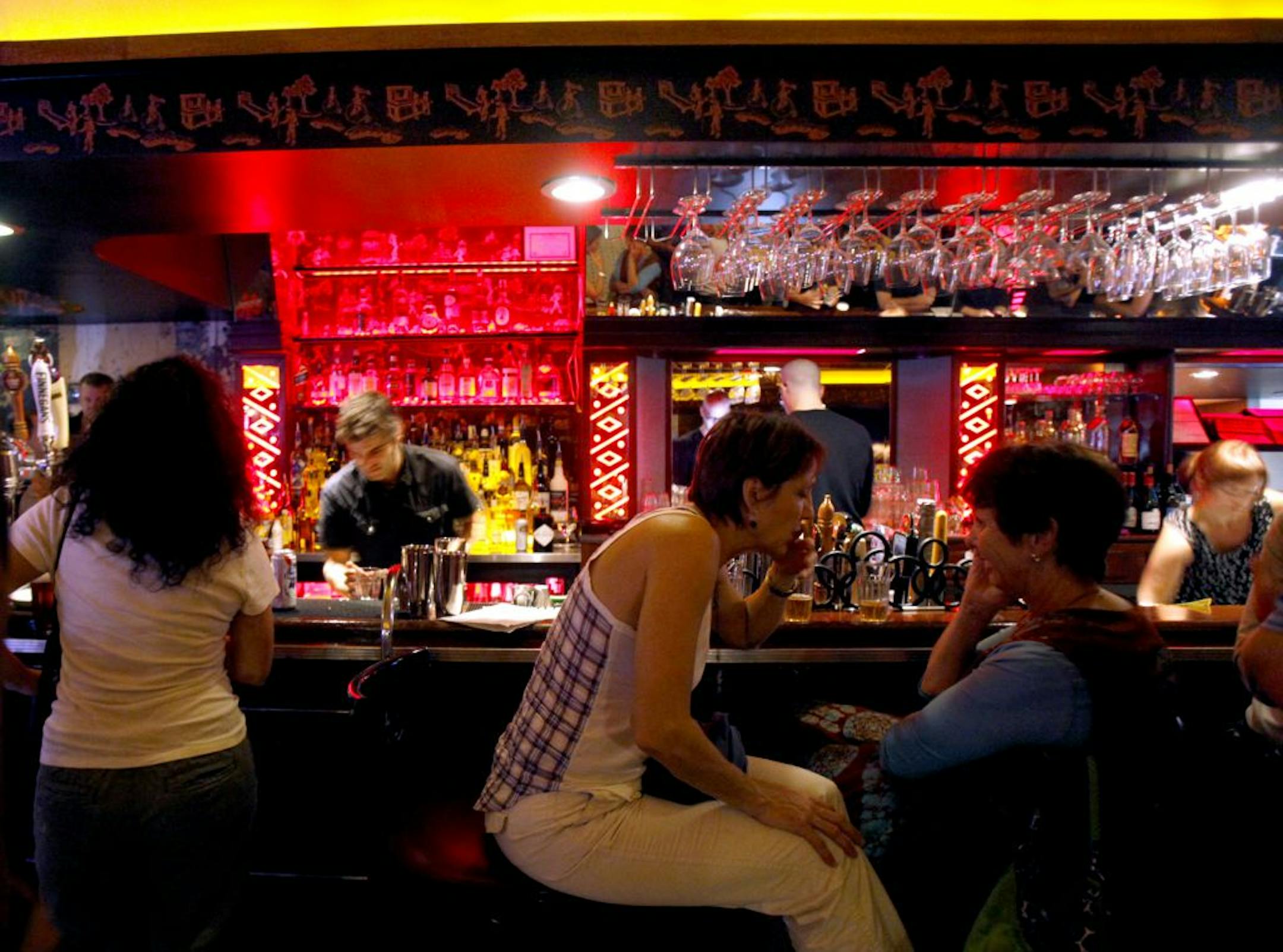 Bartender Chris Smiar pours drinks at the bar as Martha Griffin (plaid shirt) has a shot at Pat's Tap with friend Dawn Chapman looking on.