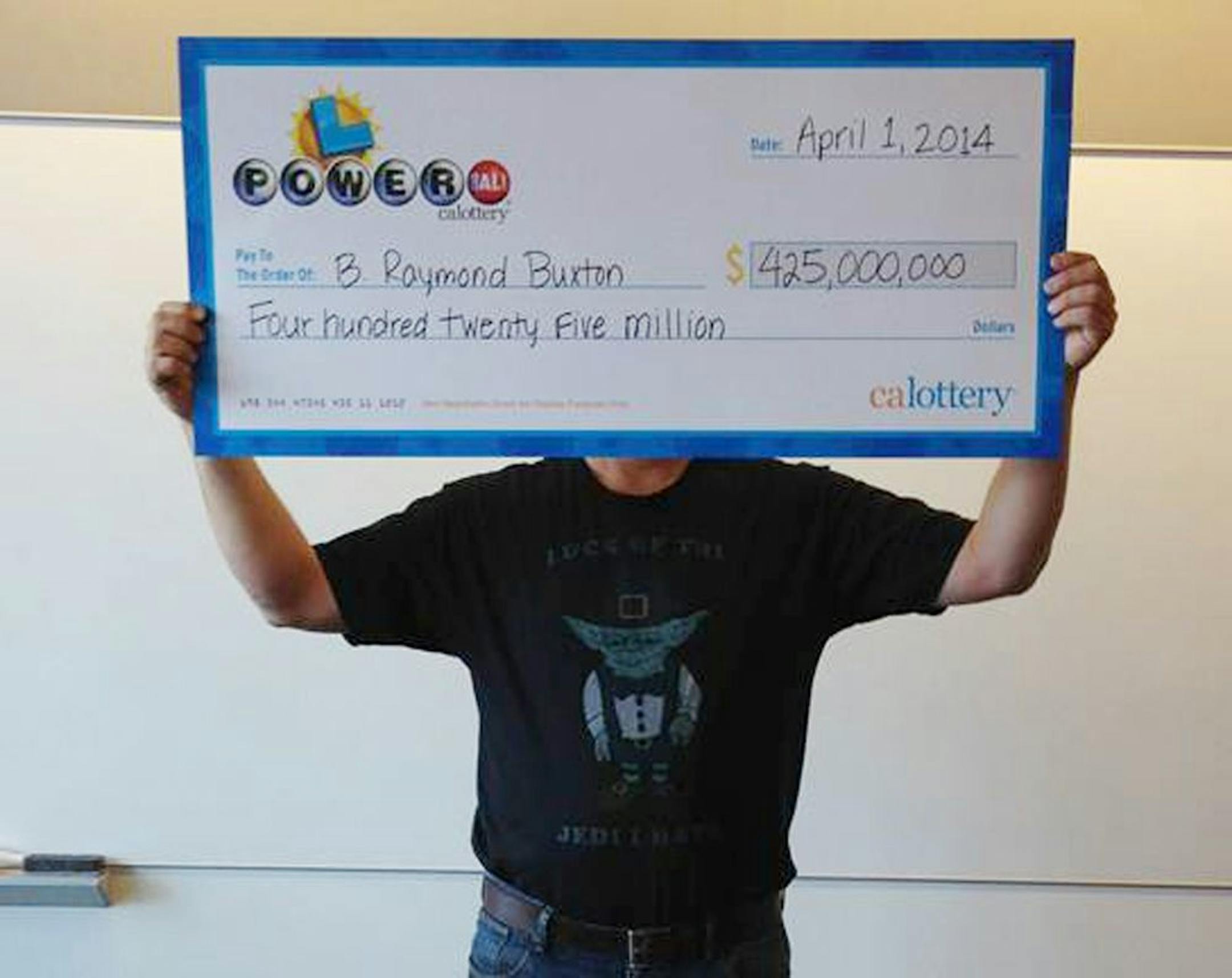 This photo provided by the California Lottery shows Powerball winner B. Raymond Buxton holding a check for $425 million, Tuesday, April 1, 2014, in Sacramento, Calif.