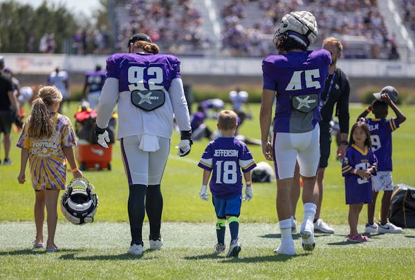 Vikings players James Lynch, left, and Troy Dye, right, get a little help with their equipment from young fans as they make their way onto the practic
