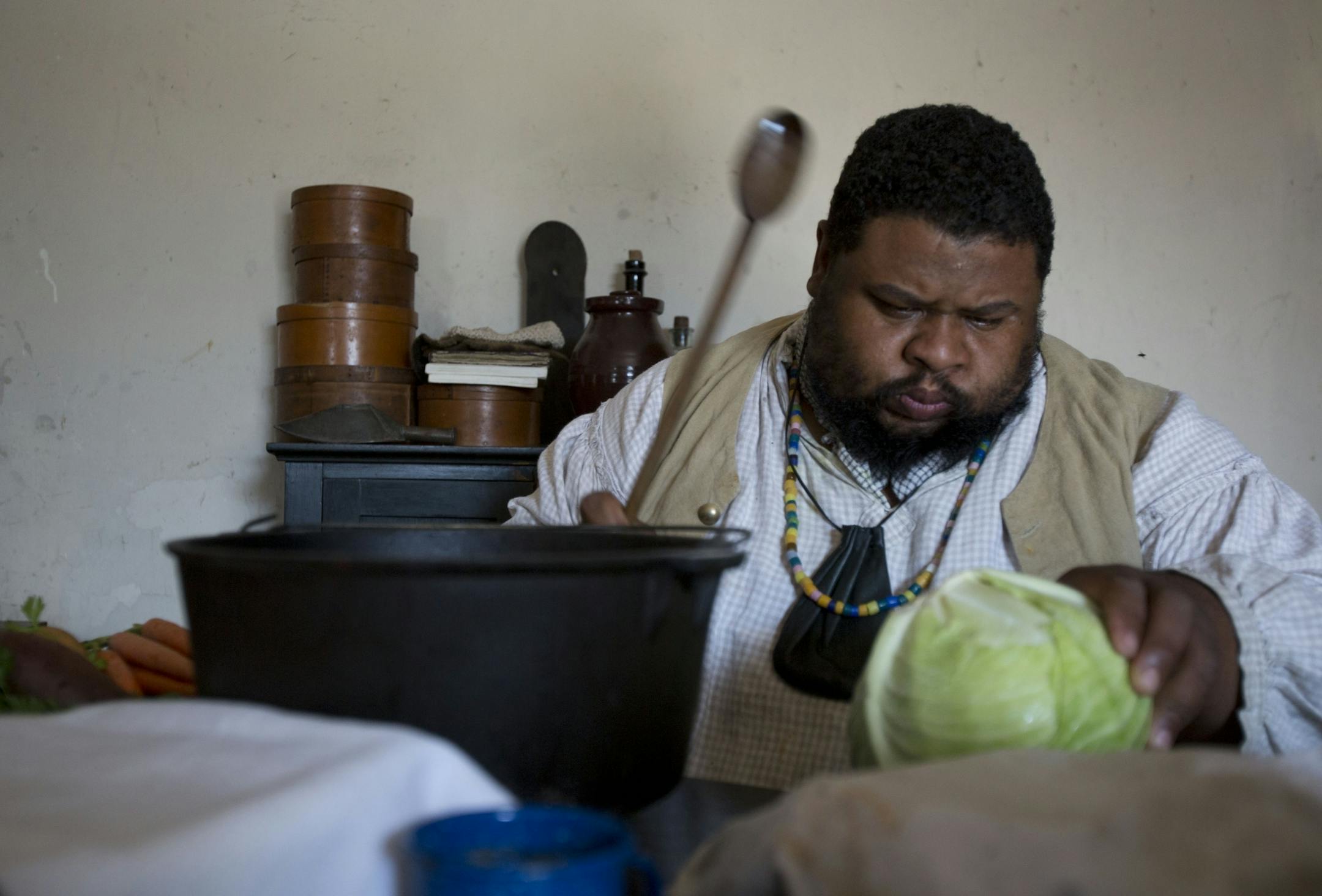 Michael Twitty beats a cabbage with a large spoon to test it's ripeness.