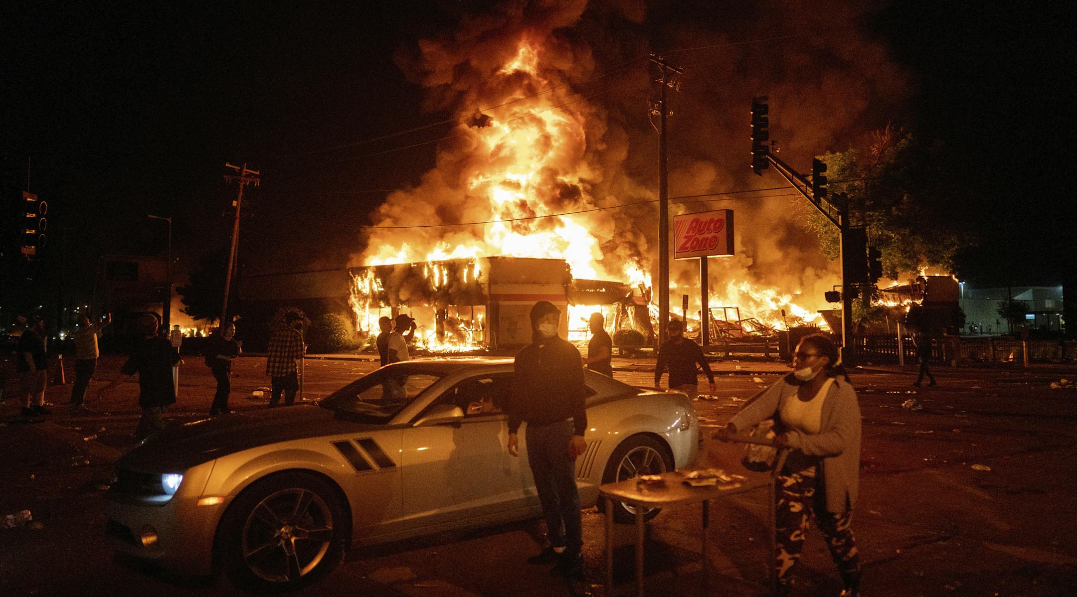 An AutoZone store burns as protesters gather outside of the Third Precinct in Minneapolis Thursday, May 28, 2020. Police say a man captured on surveillance video breaking windows at a south Minneapolis auto parts store in the days after George Floyd's death is a Hell's Angels member who was bent on stirring up social unrest. Minneapolis police spokesman John Elder told The Associated Press on Tuesday, July 28, 2020 that the investigation remains open and active and that he could not confirm the