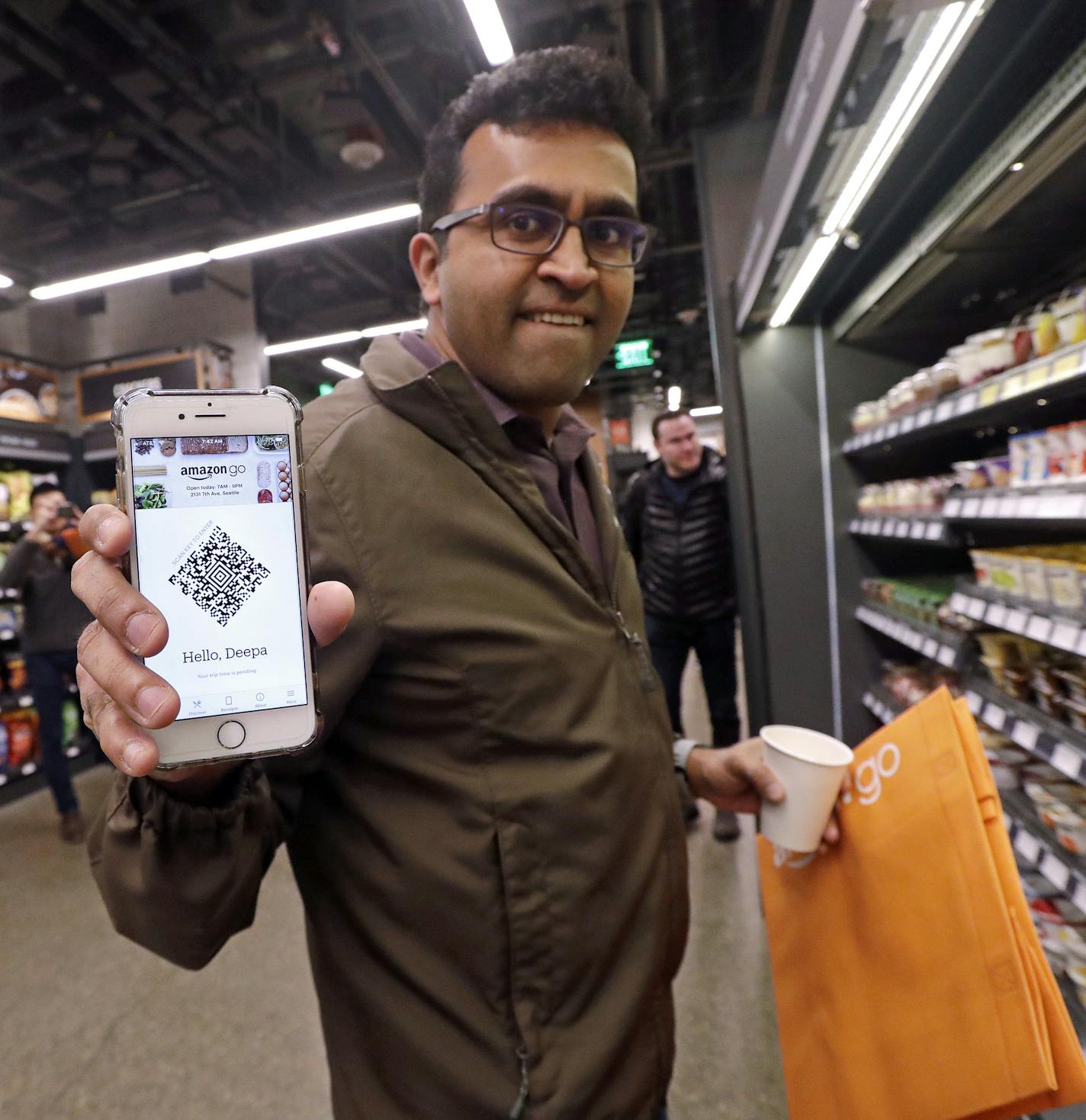 Amazon employee Krishna Iyer shows off an Amazon Go app as he shops in the store, Monday, Jan. 22, 2018, in Seattle. The store allows shoppers to scan their smartphone with the Amazon Go app at a turnstile, pick out the items they want and leave. The online retail giant can tell what people have purchased and automatically charges their Amazon account. (AP Photo/Elaine Thompson)