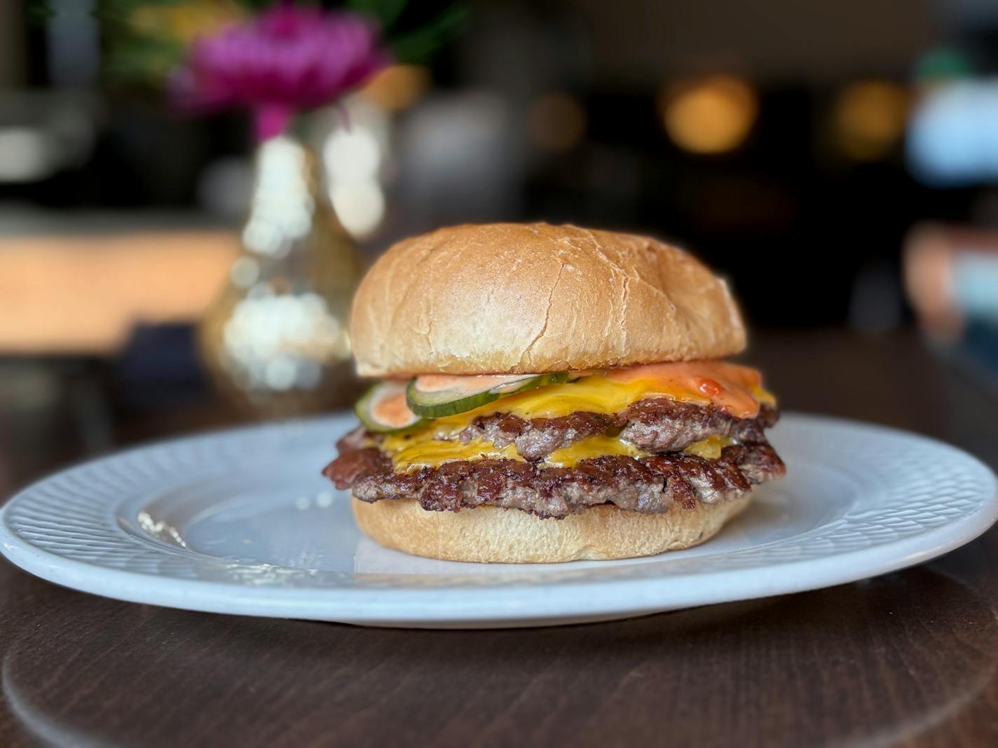 A double stacked burger topped with melty cheese, burger sauce and thick cut house pickles on a white bread bun served on a white plate inside the restaurant.