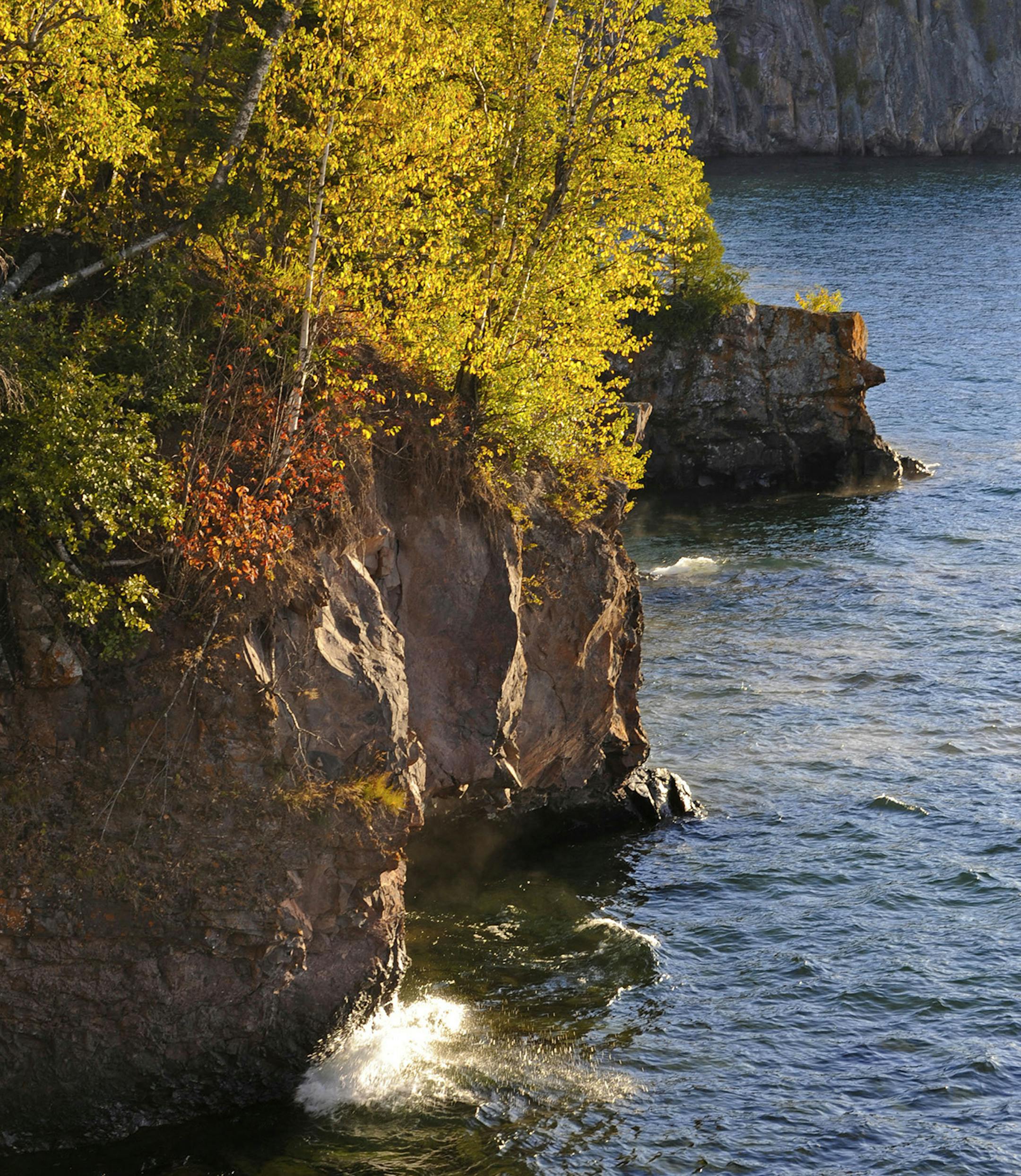 In a Sept. 30, 2009 photo,the setting sun highlights fall trees as a wave smashes into the rock at Tettegouche State Park along the shoreline of the North Shore of Lake Superior in Minnesota. (AP Photo/Jim Mone) ORG XMIT: APSTK