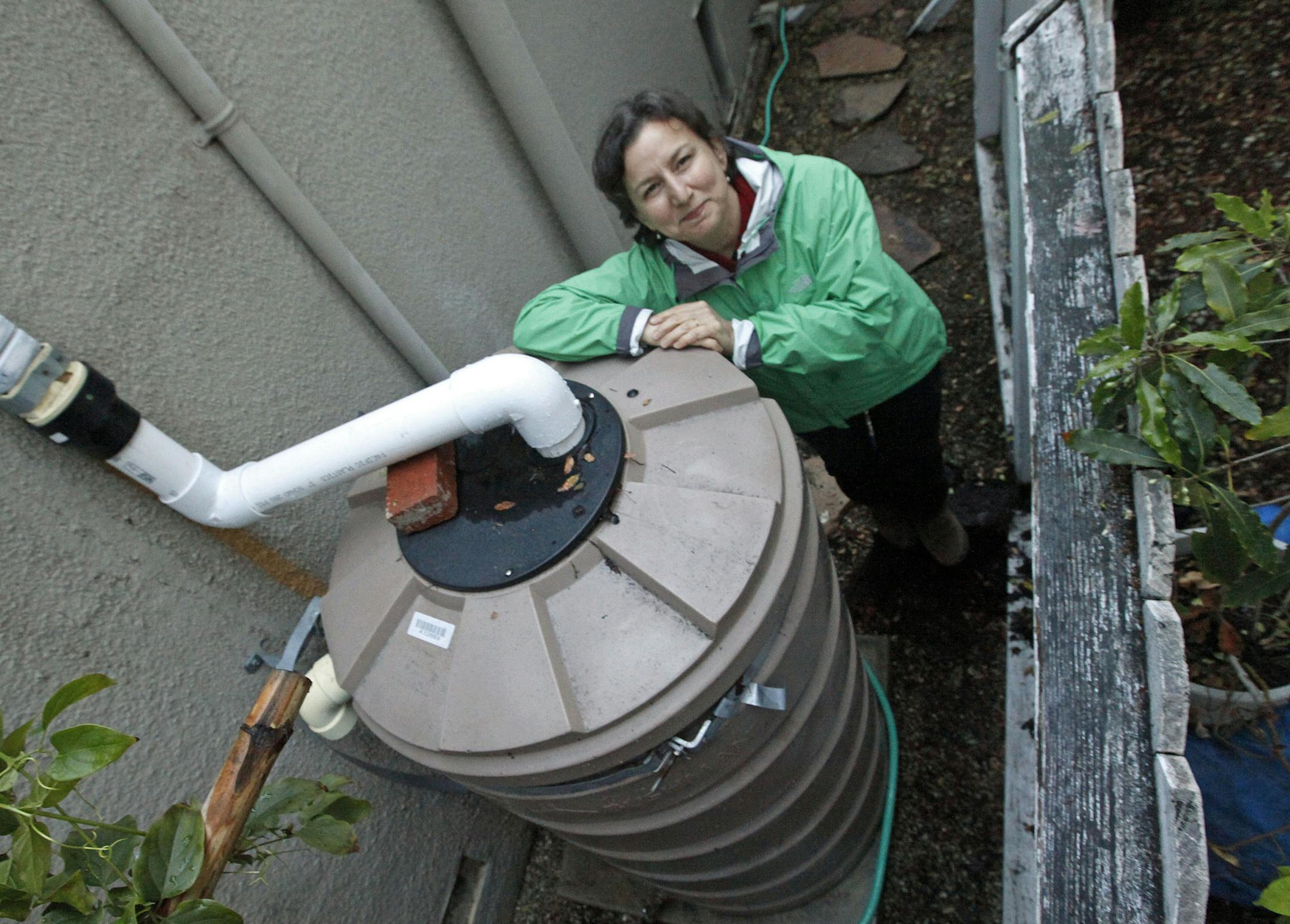 In this Feb. 28, 2014 photo, Santa Monica, Calif., resident Josephine Miller stands next to her 200-gallon water storage tank that collects rain from her home's roof to water her garden. With California in a drought, some communities in recent years have turned to water conservation measures in an effort to cut down on imported water. (AP Photo/Reed Saxon)