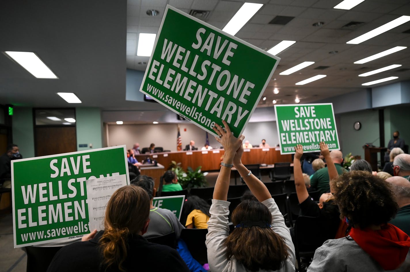 Liz Hucke, center, a pre-k Spanish dual immersion teacher at Wellstone, holds a "Save Wellstone Elementary" sign during a St. Paul School Board meeting Thursday, Nov. 11, 2021 in St. Paul, Minn. Emotions are running high among families facing potential closure of their schools in St. Paul and for board members who will decide the fate of the Envision SPPS plan next week. Board Member Zuki Ellis, looking back on a conversation this week with colleague Jessica Kopp, said: "Neither of us are sleeping well." The state's second-largest district proposes to close and shutter five schools, and merge or repurpose several others. The administration will have its final recommendation in writing on Friday, and signs point to no major changes in the plan introduced in October. ] AARON LAVINSKY • aaron.lavinsky@startribune.com