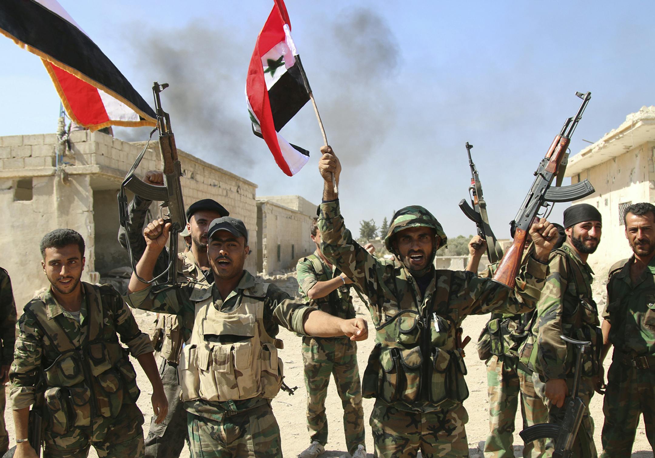 In this photo taken on Sunday, Oct. 11, 2015, Syrian soldiers waving Syrian flags celebrate the ?apture of Achan, Hama province, Syria. Russian jets intensified their airstrikes Monday in the central Syrian province as government and allied troops pushed out insurgents from local villages to expand their control of the area, activists and a military statement said.