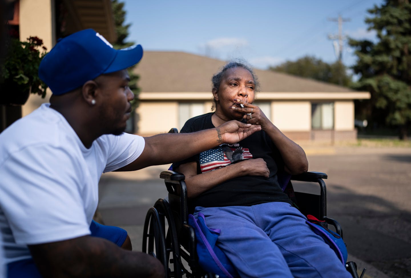 Marvin Haynes holds his hand under his mother Sharon Shipp's cigarette to catch the ash while visiting her nursing home in Minneapolis, Minn. on Thursday, July 25, 2024. 