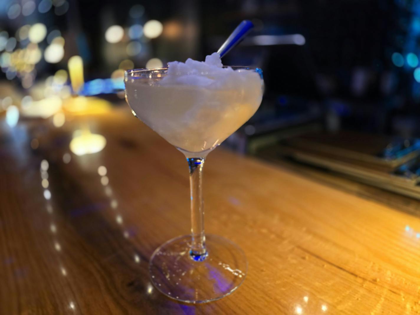 A glass on a bar that has a clear liquid and a scoop of white sorbet, with a spoon sticking out