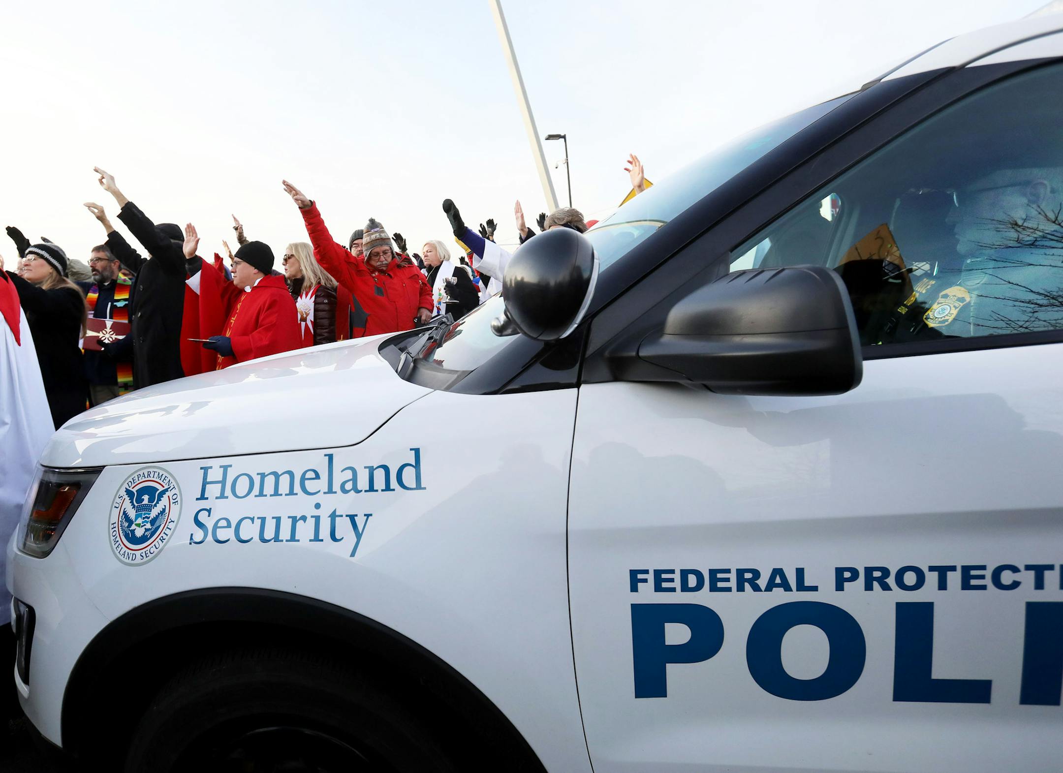 Episcopal clergy as well as clergy from other faiths open their arms in a blessing towards detainees housed in the Whipple Federal Building as a Homeland Security police officer blocked their path to the building Tuesday, Oct. 29, 2019, in St. Paul, MN. Earlier, clergy and protestors gathered for a service and communion outside the Whipple Federal Building and to protest the naming of the building after the Episcopal bishop because deportations and other actions at the courthouse are in oppositi