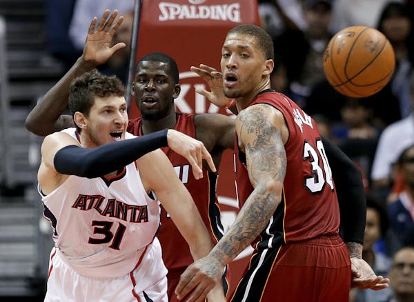 Atlanta Hawks' Mike Muscala, left, passes the ball away from Miami Heat's James Ennis, rear, and Michael Beasley during the fourth quarter of an NBA b