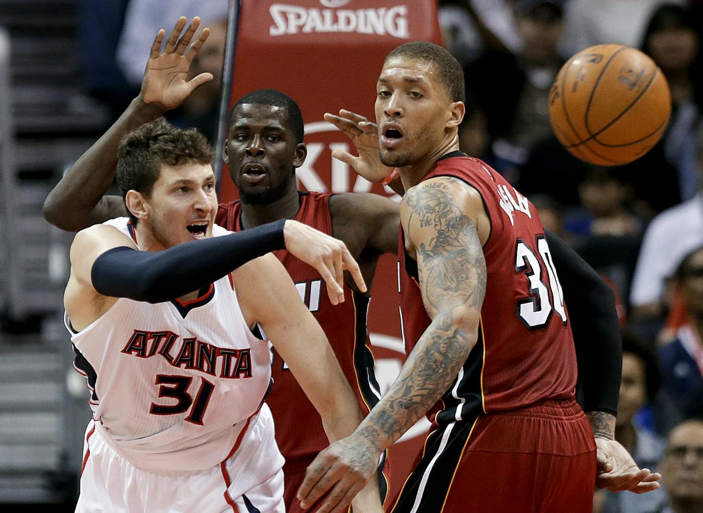 Atlanta Hawks' Mike Muscala, left, passes the ball away from Miami Heat's James Ennis, rear, and Michael Beasley during the fourth quarter of an NBA basketball game Friday, March 27, 2015, in Atlanta. The Hawks won 99-86. (AP Photo/David Goldman)