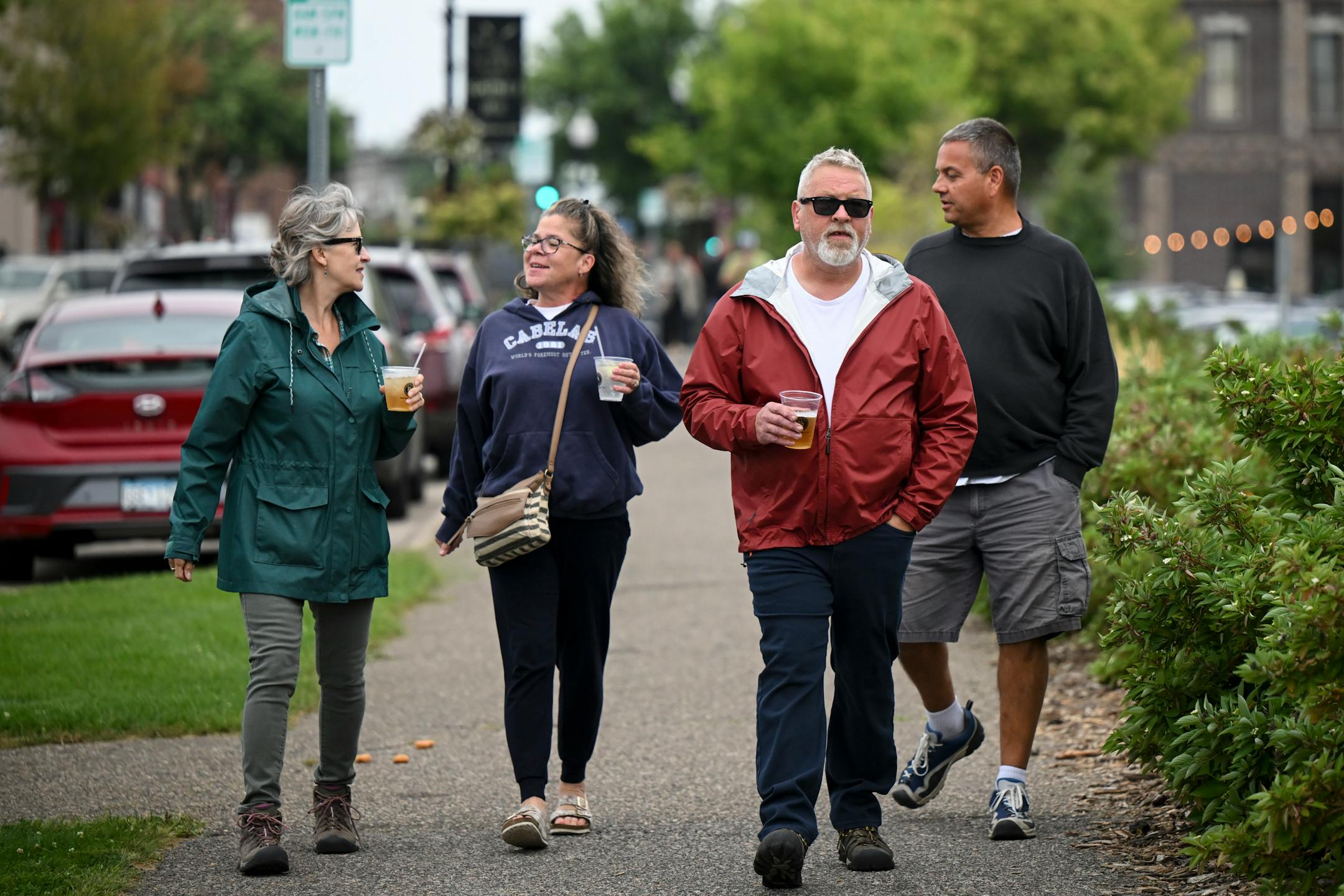 From left, Jill Neitzel, Brenda Tresco, James Neitzel and Jeff Tresco walk toward Riverfront Memorial Park with drinks from 201 Tavern in downtown Anoka Wednesday, Sept. 6, 2023 in Anoka, Minn. Starting Wednesday, anybody 21 and older may buy adult beverages from some bars and restaurants in Anoka and consume them as they walk on sidewalks, into shops that allow it, and along the riverfront in the city's historic downtown. The social district will pilot a project as a way to generate activity and bring people together. ] AARON LAVINSKY • aaron.lavinsky@startribune.com