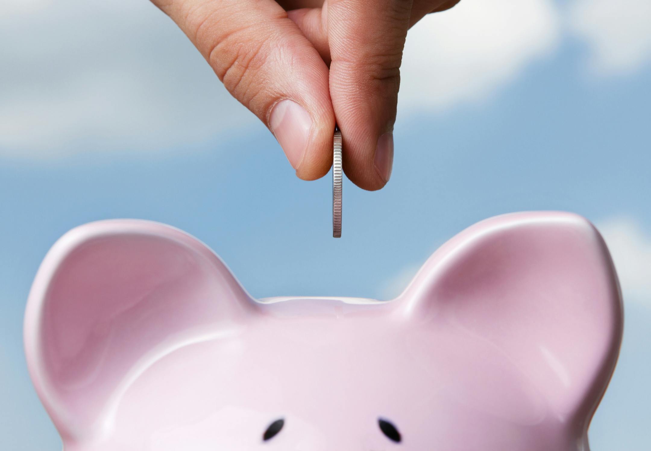 Male hand putting a coin into piggy bank