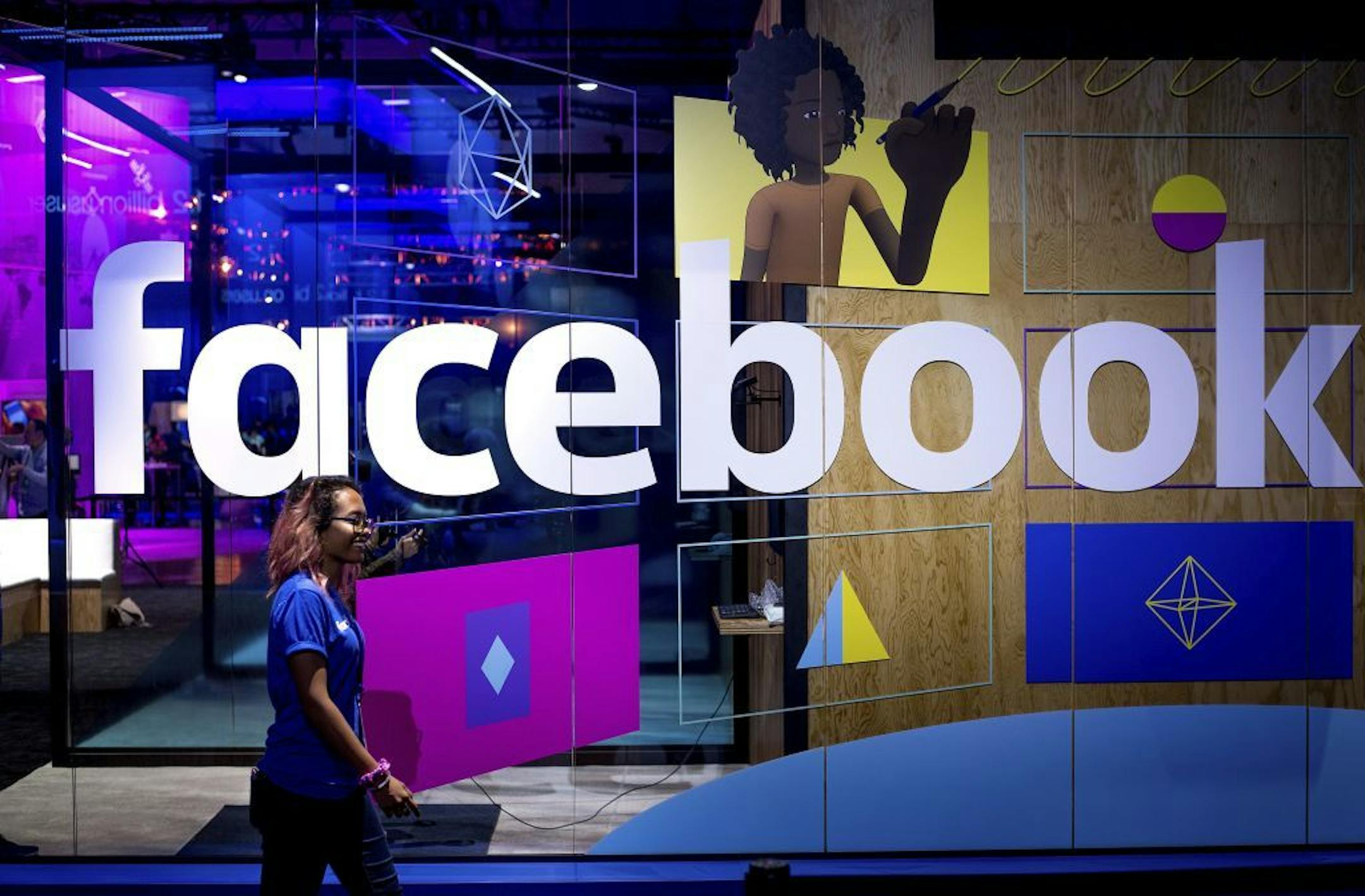 FILE - In this Tuesday, April 18, 2017, file photo, a conference worker passes a demo booth at Facebook's annual F8 developer conference, in San Jose, Calif. Facebook says it is changing how it identifies "fake news" stories on its platform to a more effective system. The social-media network had put "disputed" labels on stories that fact-checkers found false. Instead, now it will bring up "related articles" next to the false stories that give context from fact-checkers on the stories' problems.