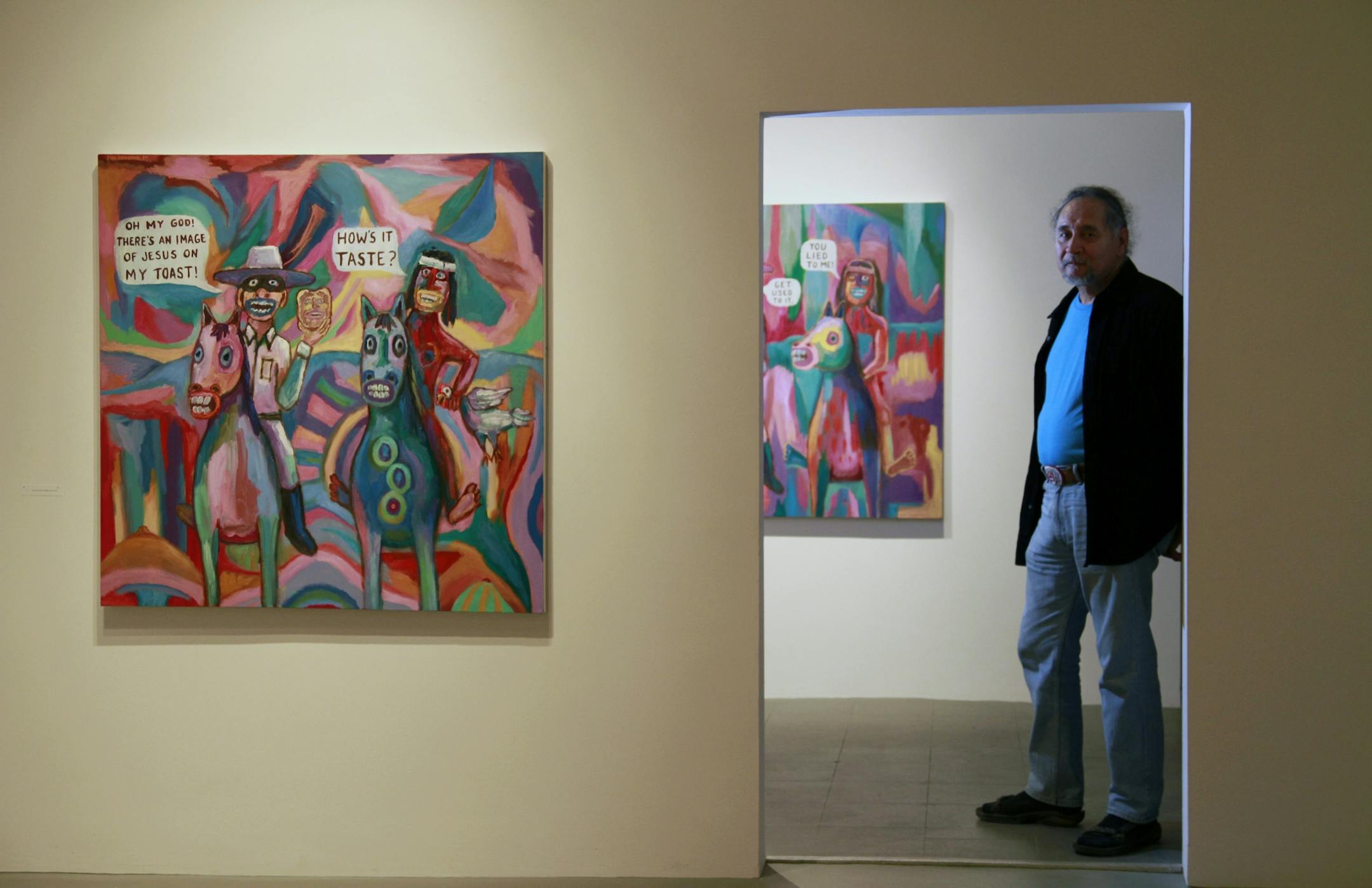 Artist Jim Denomie, framed amidst his oil paintings on display at the Bockley Gallery in Minneapolis.