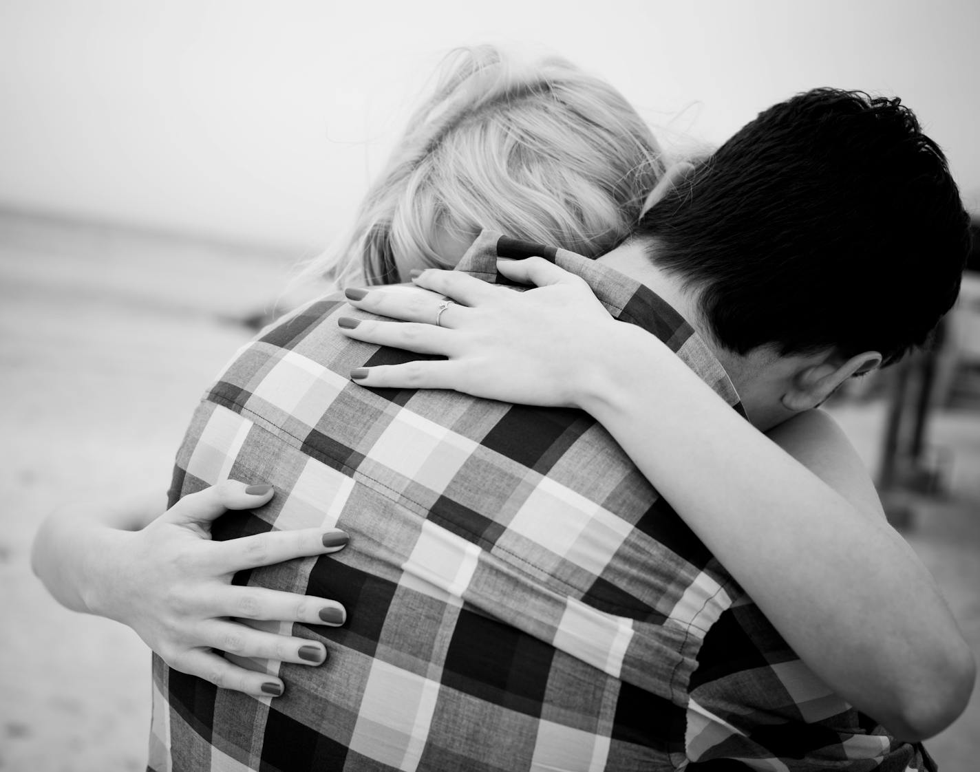 The back view of a couple embracing at the beach. No visible faces showing. Black and white image.