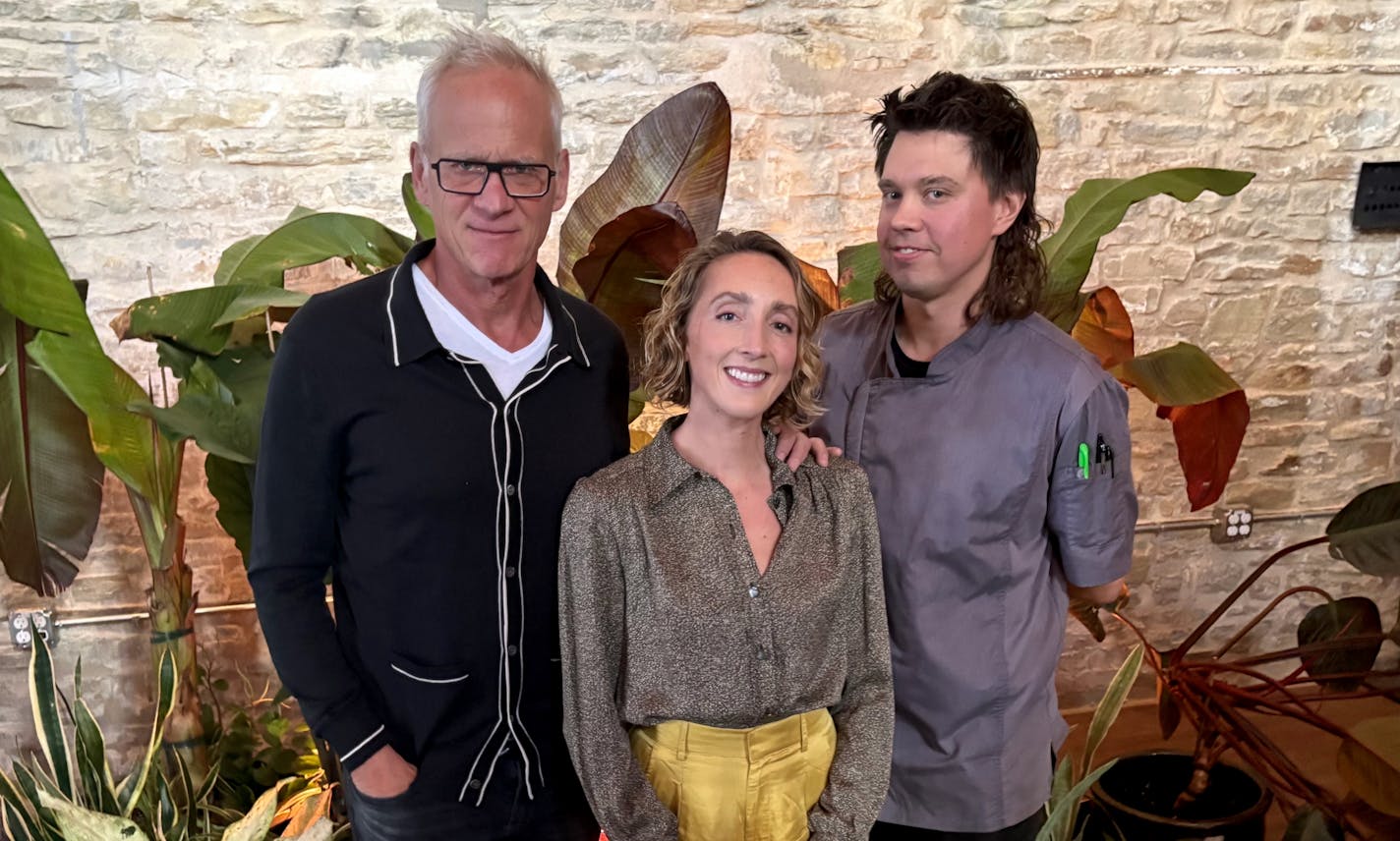 Aster House owner Jeff Arundel, consulting chef Karyn Tomlinson and chef Josh Jones photographed inside the dining room, standing in front of a brick wall next to some tropical plants.