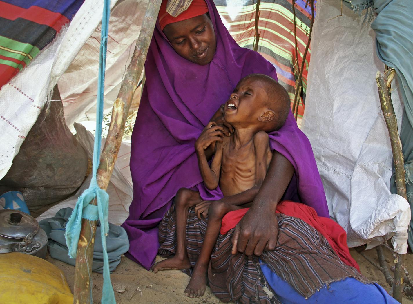 In this photo taken Tuesday, March 28, 2017, newly displaced Somali mother Sahra Muse, 32, comforts her malnourished child Ibrahim Ali, 7, in their makeshift shelter at a camp in the Garasbaley area on the outskirts of Mogadishu, Somalia. Drought-stricken families facing a hunger crisis are on the move, trying to reach international aid agencies that cannot distribute food in areas under the control of al-Shabab, Somalia's homegrown Islamic extremist rebels who are affiliated to al-Qaida. (AP Ph