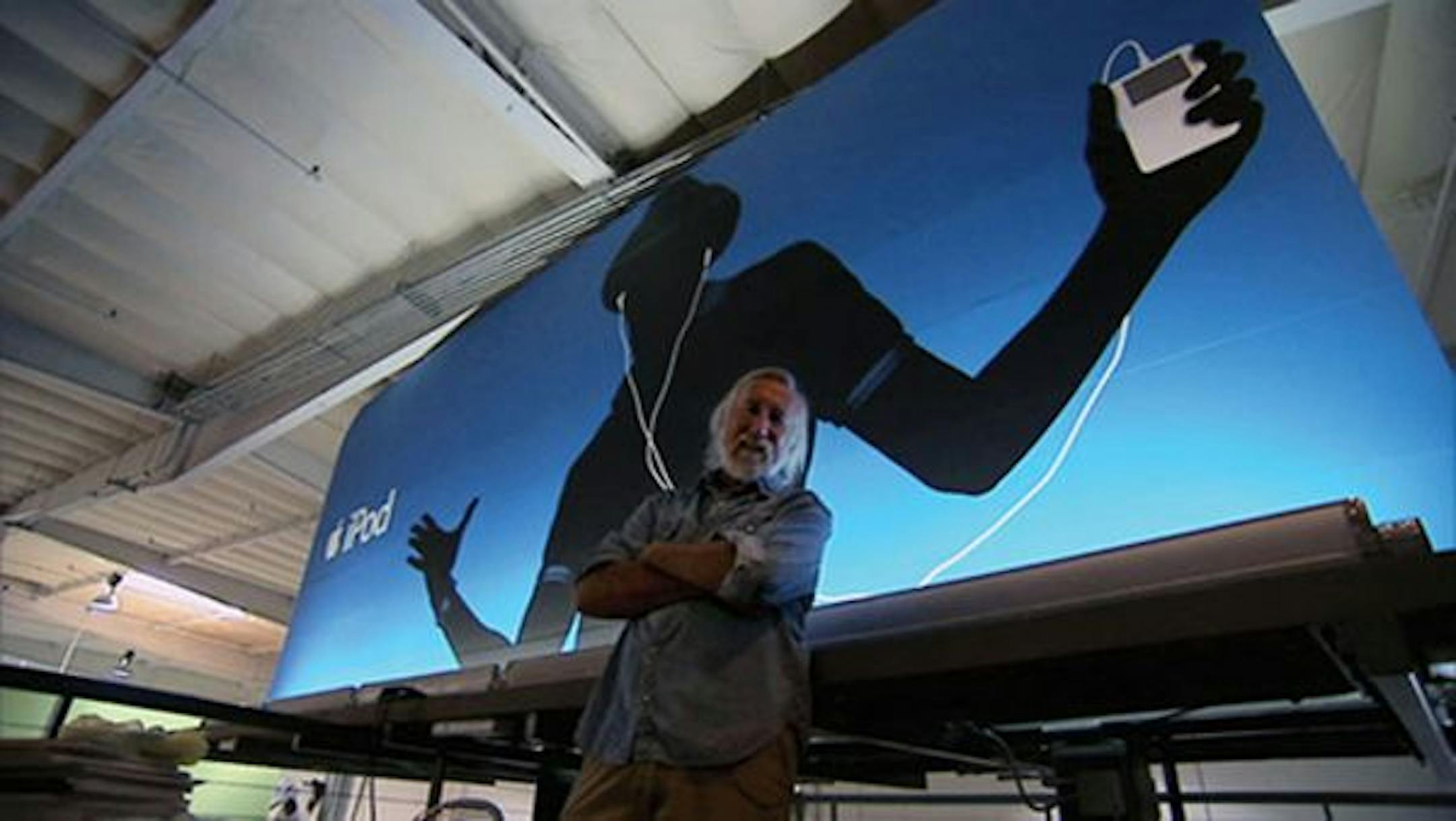 Lee Clow, surfer and chairman and chief creative officer of TBWA WorldwideChiatDay, in front of a full-size iPod billboard inside the Los Angeles office. Clow has been largely responsible for Apple's ad campaigns since 1984. From the film ART & COPY directed by Doug Pray. Credit: Still from the movie.