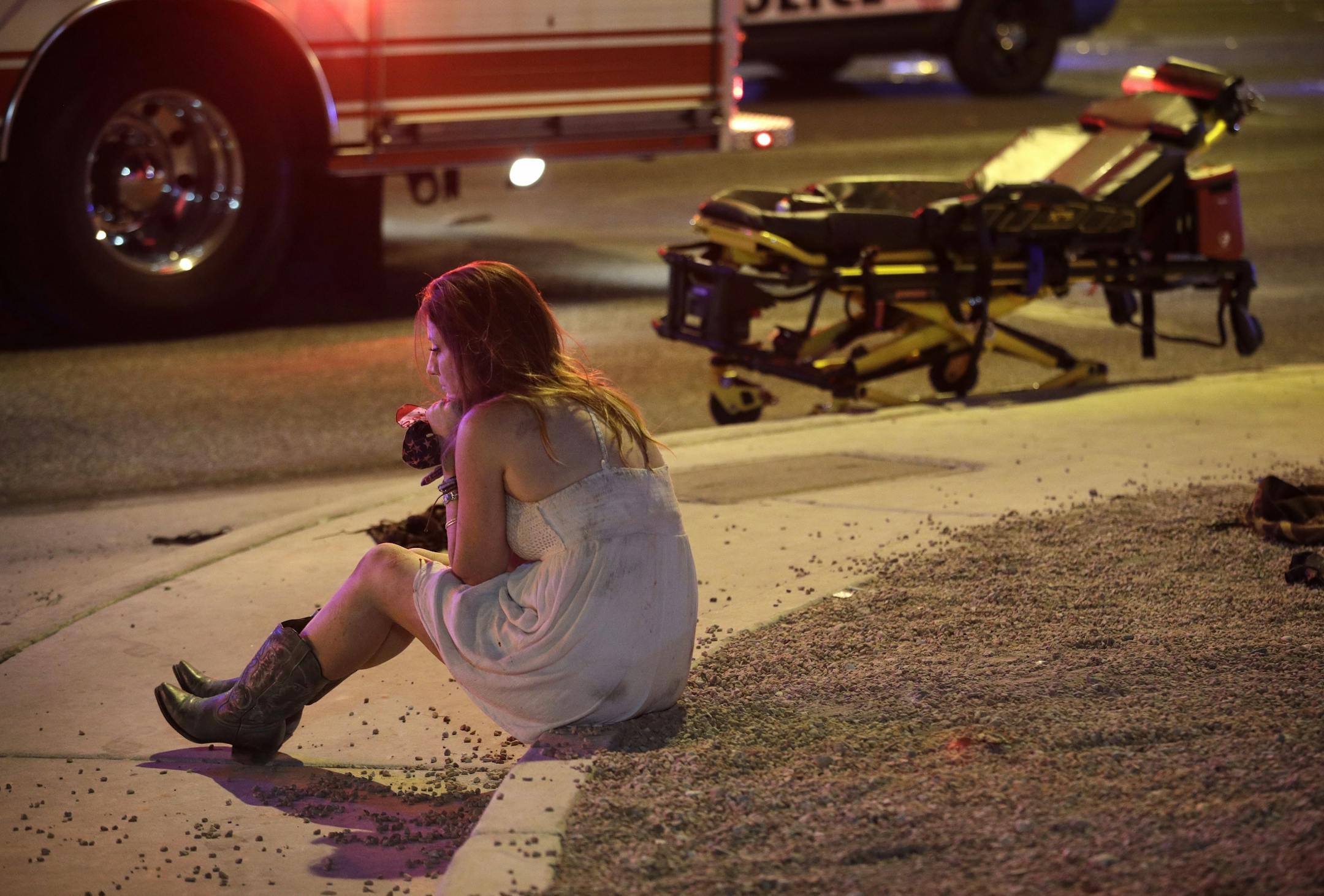 A woman sits on a curb at the scene of a shooting outside of a music festival along the Las Vegas Strip, Monday, Oct. 2, 2017, in Las Vegas.
