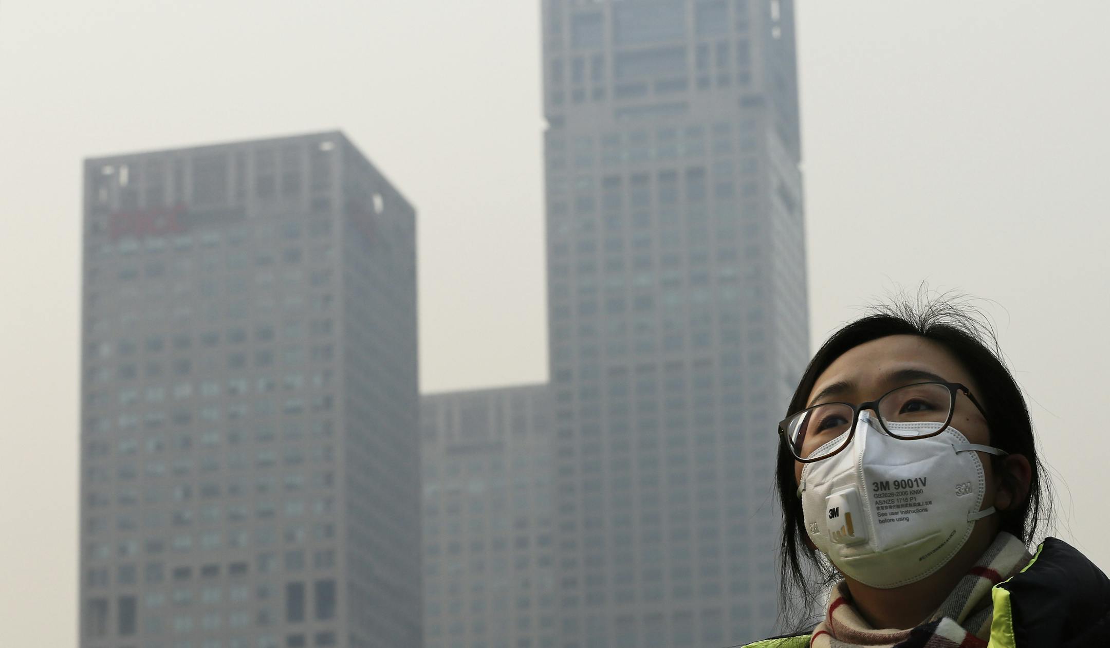 A woman wearing a face mask to protect herself from pollutants walks past office buildings shrouded with pollution haze in Beijing, Monday, Dec. 7, 2015. Beijing issued its first-ever red alert for smog on Monday, urging schools to close and invoking restrictions on factories and traffic that will keep half of the city's vehicles off the roads. (AP Photo/Andy Wong)
