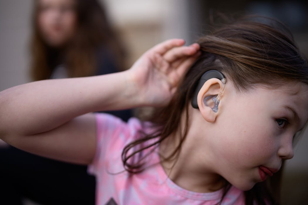 Zoey Voigt, 10, shows one of her cochlear implants while sitting next to her sister, Abigail, in their driveway Wednesday in St. Augusta.