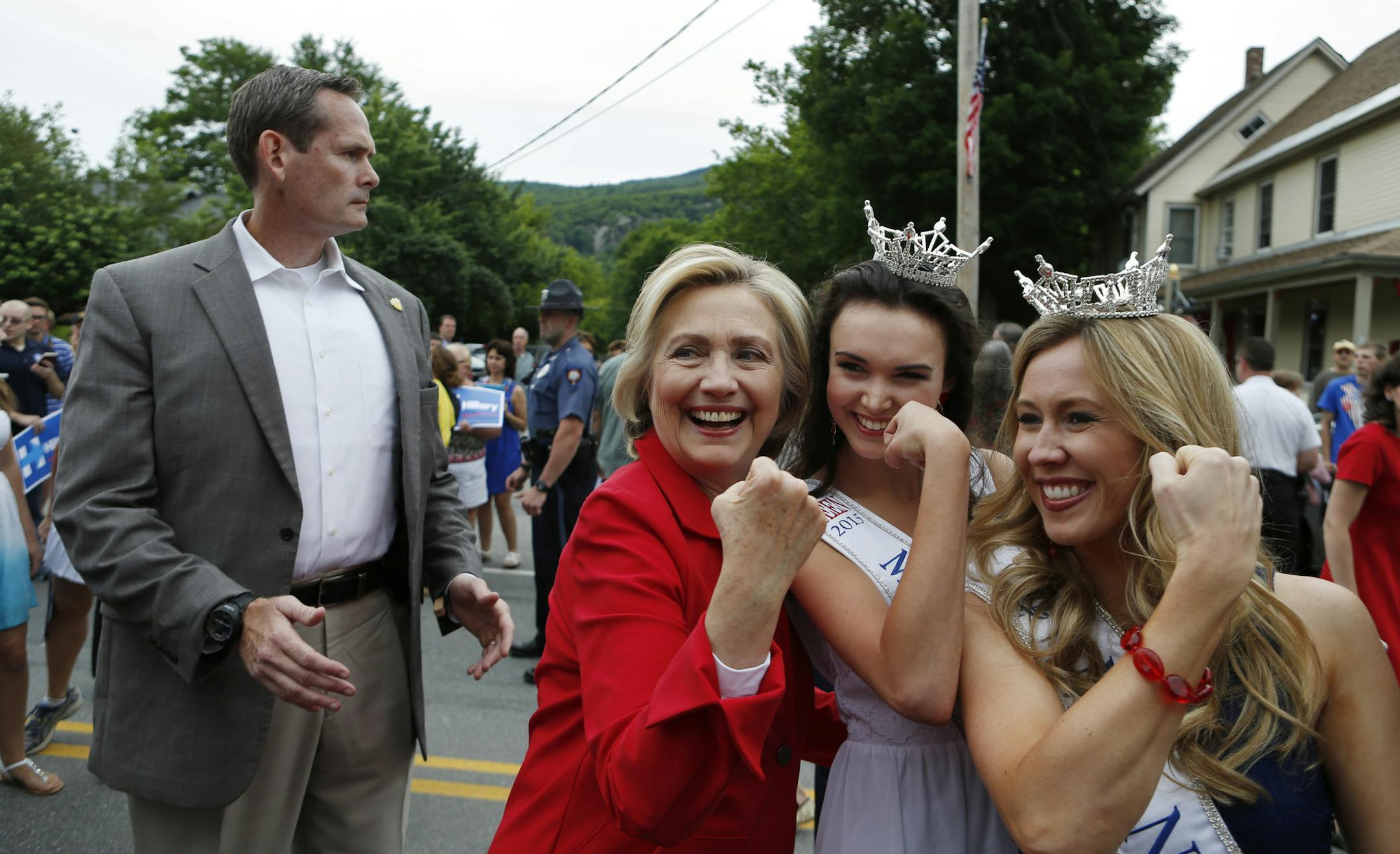 A Secret Service agent watches as Democratic presidential candidate Hillary Rodham Clinton flexes her muscle with Miss Teen New Hampshire Allie Knault, center, and Miss New Hampshire Holly Blanchard, during a parade, Saturday, July 4, 2015, in Gorham, N.H. (AP Photo/Robert F. Bukaty)
