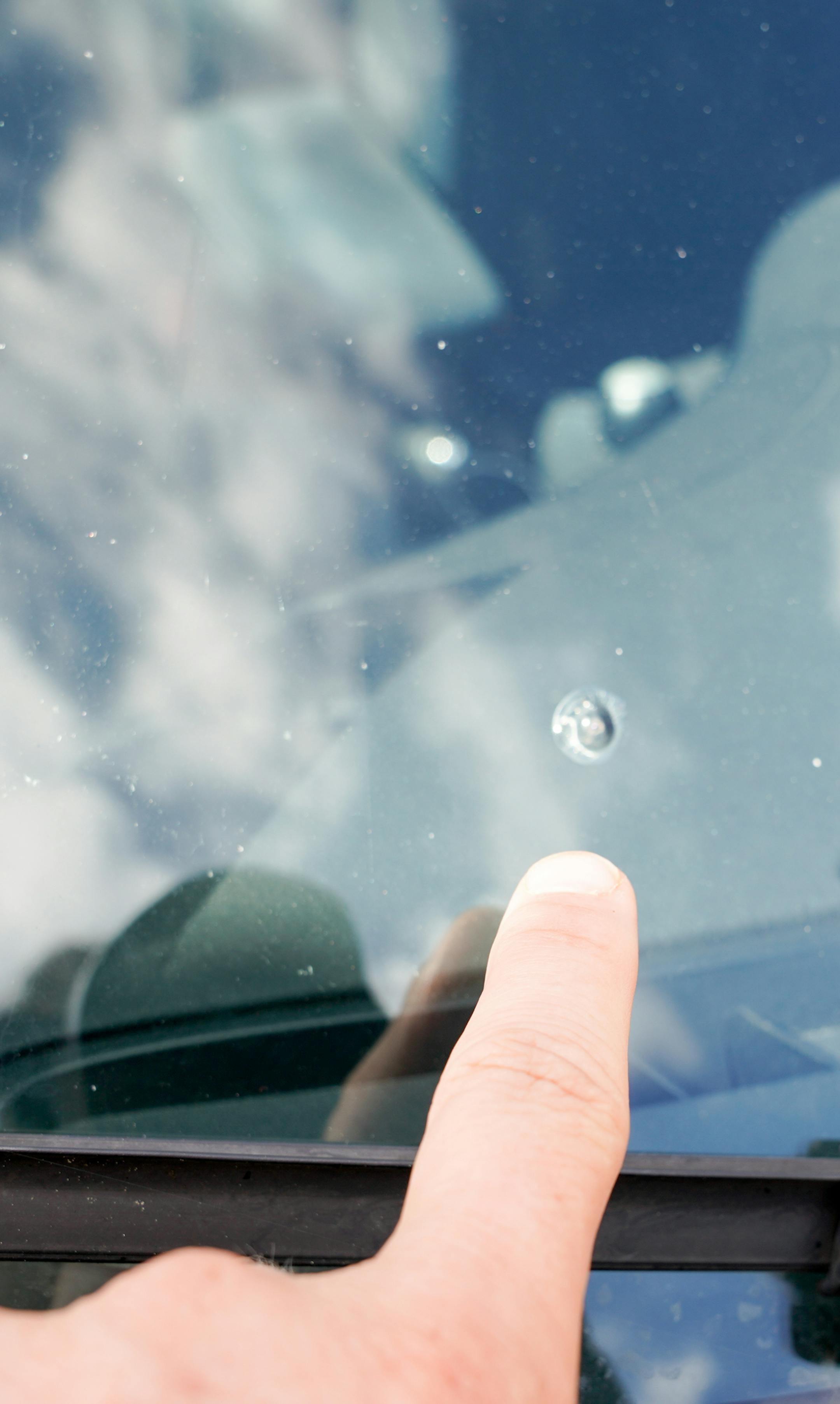 finger hand man pointing broken windshield of a car traces of oncoming stone on road