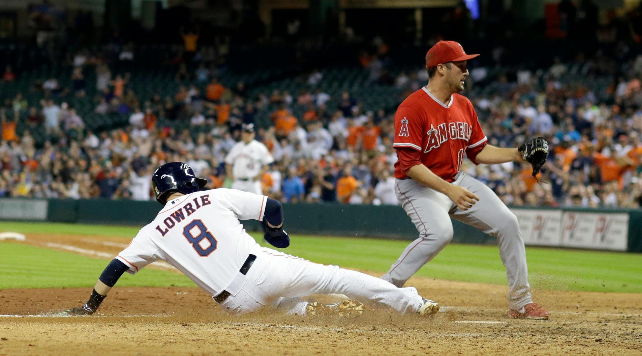 Houston Astros' Jed Lowrie (8) slides safely across home plate to score on a wild pitch thrown by Los Angeles Angels' Huston Street, right, during the eighth inning of a baseball game Tuesday, Sept. 22, 2015, in Houston. (AP Photo/David J. Phillip)