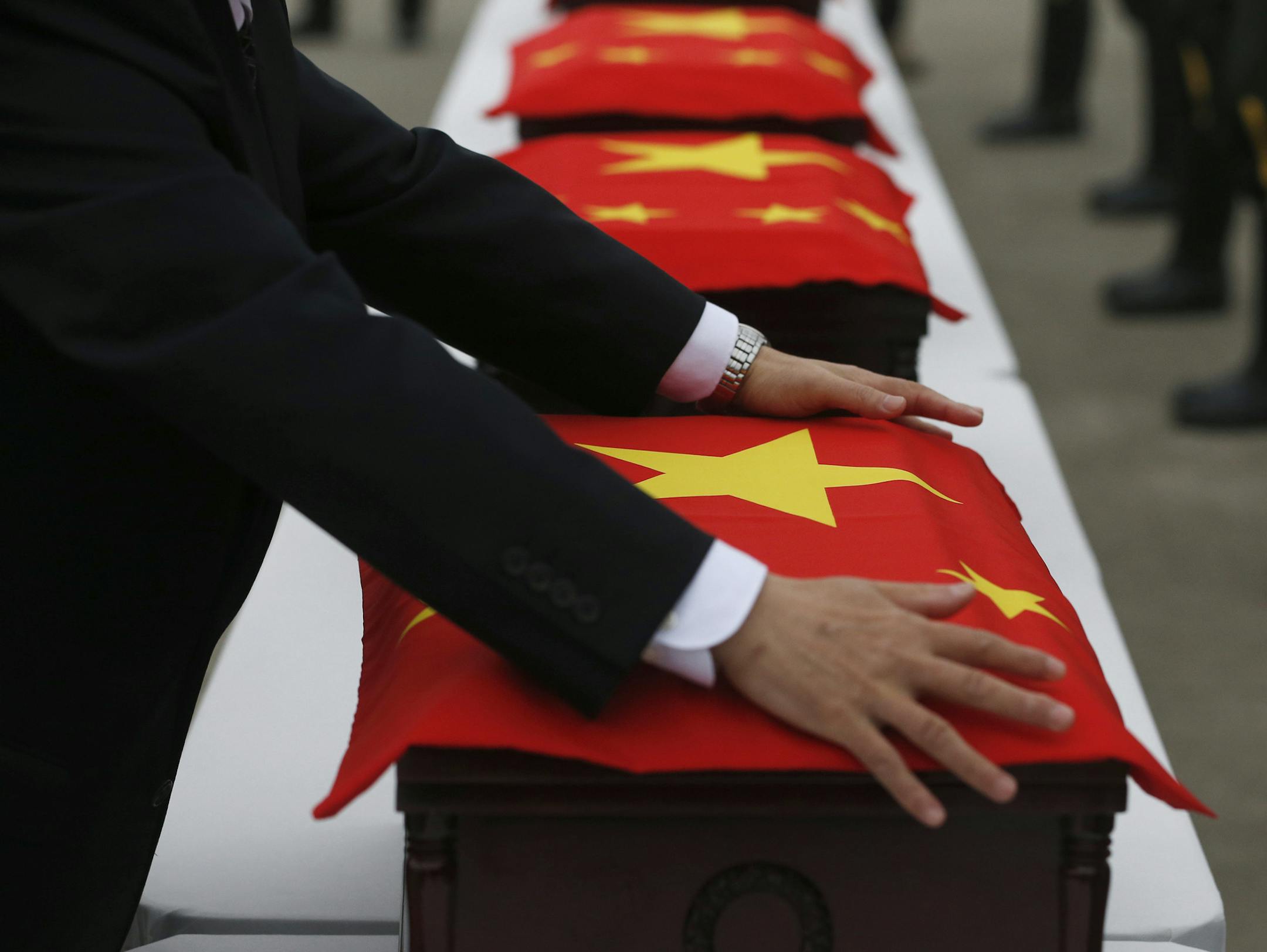 Chinese Ambassador to South Korea Qiu Guohong covers caskets containing the remains of Chinese soldiers with a Chinese national flag during the handing over ceremony of the remains at the Incheon International Airport in Incheon, South Korea Friday, March 28, 2014. The remains of more than 400 Chinese soldiers killed during the 1950-53 Korean War were transferred from the temporary columbarium in South Korea to the airport to return home for permanent burial. (AP Photo/Kim Hong-ji, Pool)
