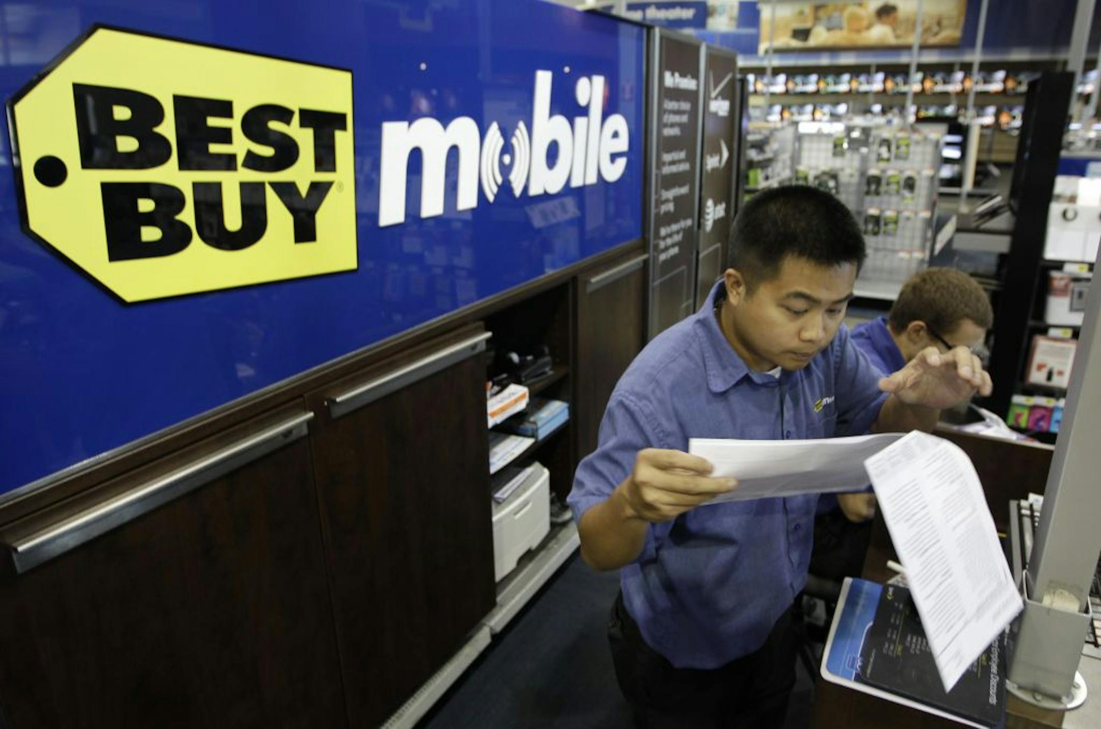 A Best Buy employee in Mountain View, Calif., looked over a cellphone contract. Best Buy's first-quarter profit dropped 26 percent on restructuring charges as the struggling electronics retailer began implementing its turnaround plan.