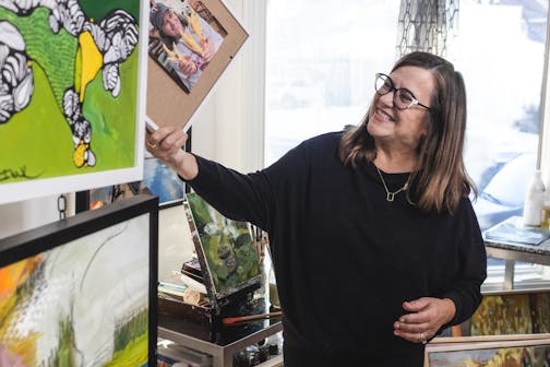 A woman laughs while holding up a framed photograph in a home art studio.