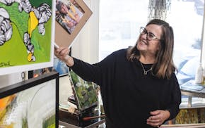 A woman laughs while holding up a framed photograph in a home art studio.