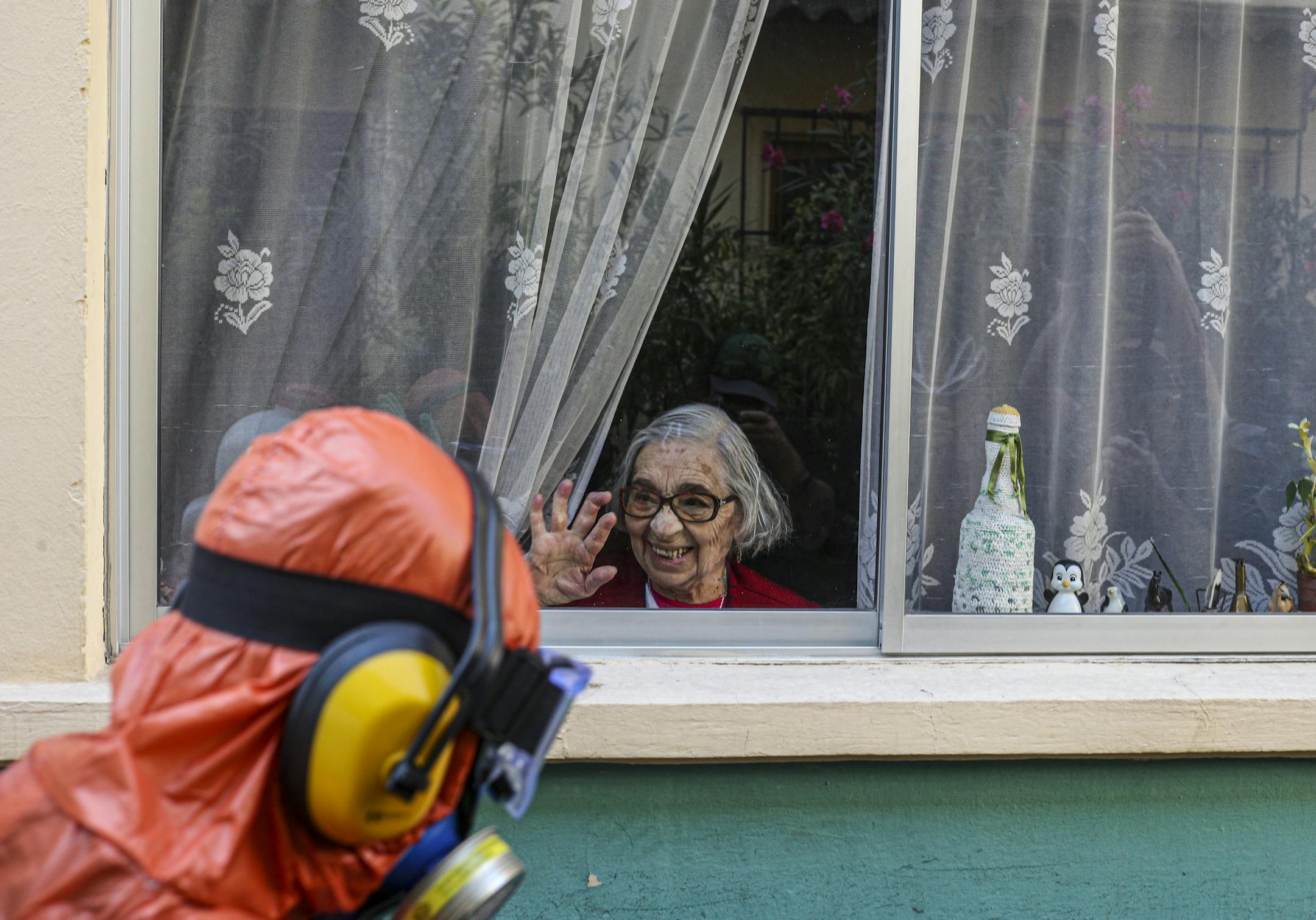 A woman waves to a city worker dressed in a hazmat suit as he disinfects the streets in her neighborhood as a precaution against the spread of the new coronavirus, in Santiago, Chile, Wednesday, April 15, 2020.