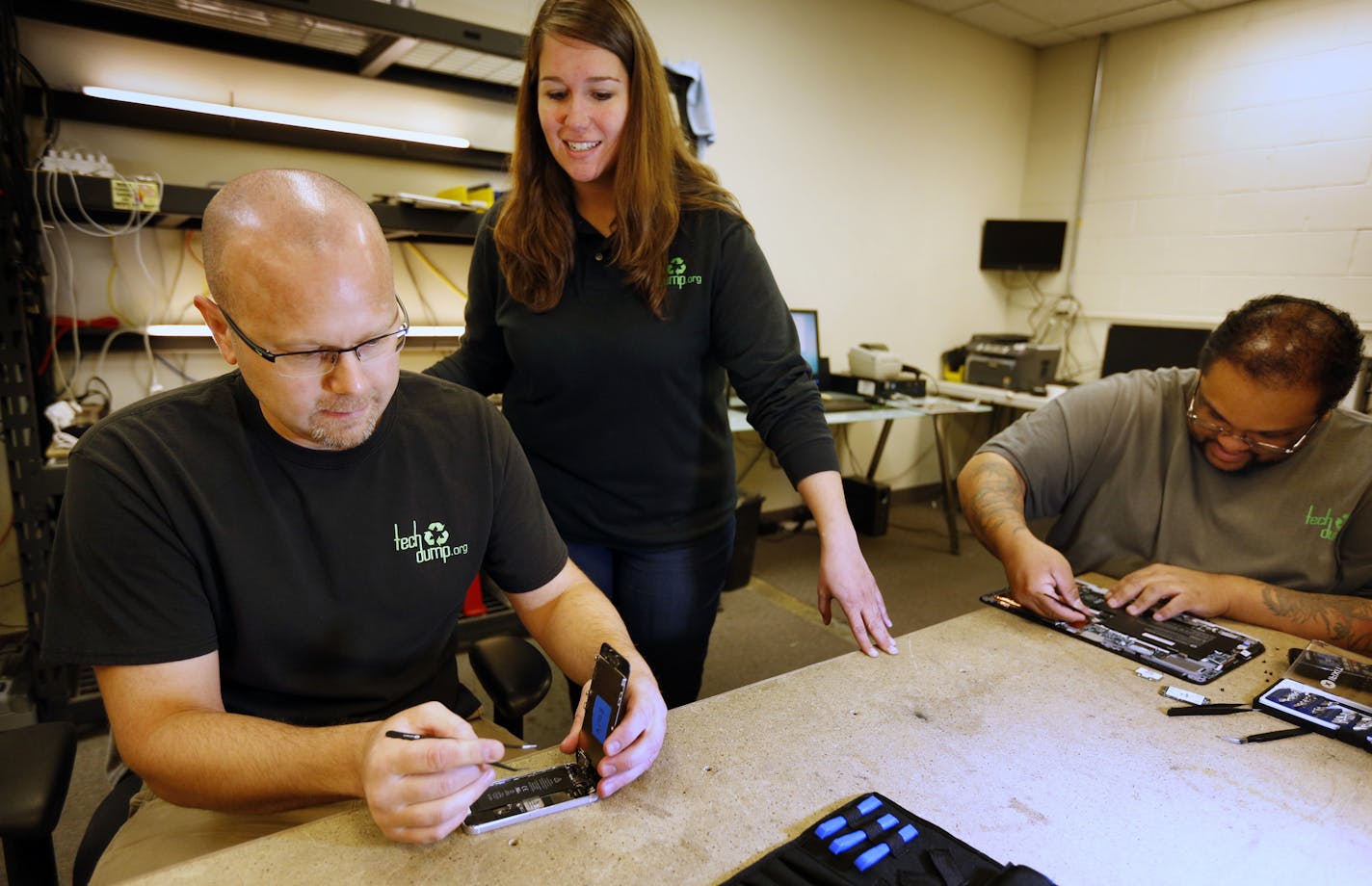 Tech Dump CEO Amanda LaGrange (center) chats with technicians Dan Saba (left) and Alonzo Nelson (right) as they work on refurbishing an iPhone and computer board. Consumer technology commands much higher prices in the resale market than recycling the metals, glass and plastics. Those commodity prices have been down for nearly two years, causing some competitors to retrench or fail. ] brian.peterson@startribune.com
Golden Valley, MN - 09/09/2016