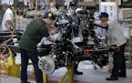Workers install an engine on a BAIC SUV chassis frame at the Chinese automaker BAIC ORU assembly plant in Beijing, Wednesday, Aug. 29, 2018. Their tar