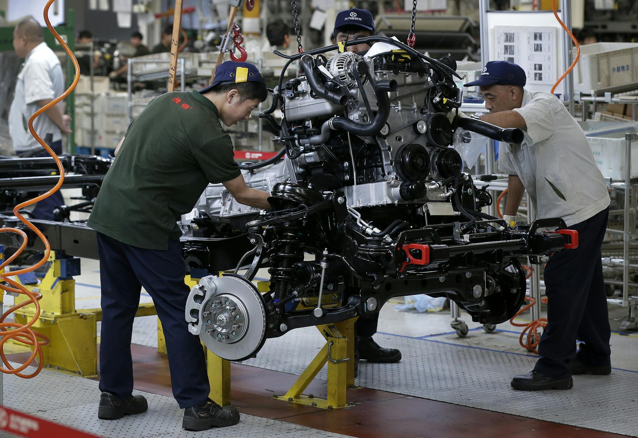 Workers install an engine on a BAIC SUV chassis frame at the Chinese automaker BAIC ORU assembly plant in Beijing, Wednesday, Aug. 29, 2018. Their tariff war with the U.S. grabs headlines, but China faces bigger economic challenges than U.S. President Donald Trump. Communist leaders who are trying to nurture more sustainable growth in the world&#xed;s No. 2 economy clamped down on bank lending to rein in surging debt. (AP Photo/Andy Wong)