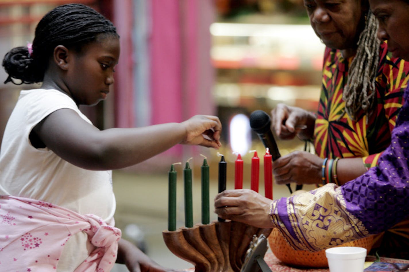 Bintou Dibba, 8, received help from Jewelean Jackson, right, and Naima Richmond as she lit the first of the Mishumaa Saba, or seven candles, during a Kwanzaa celebration at Midtown Global Market in Minneapolis Friday, Dec. 26, 2008.