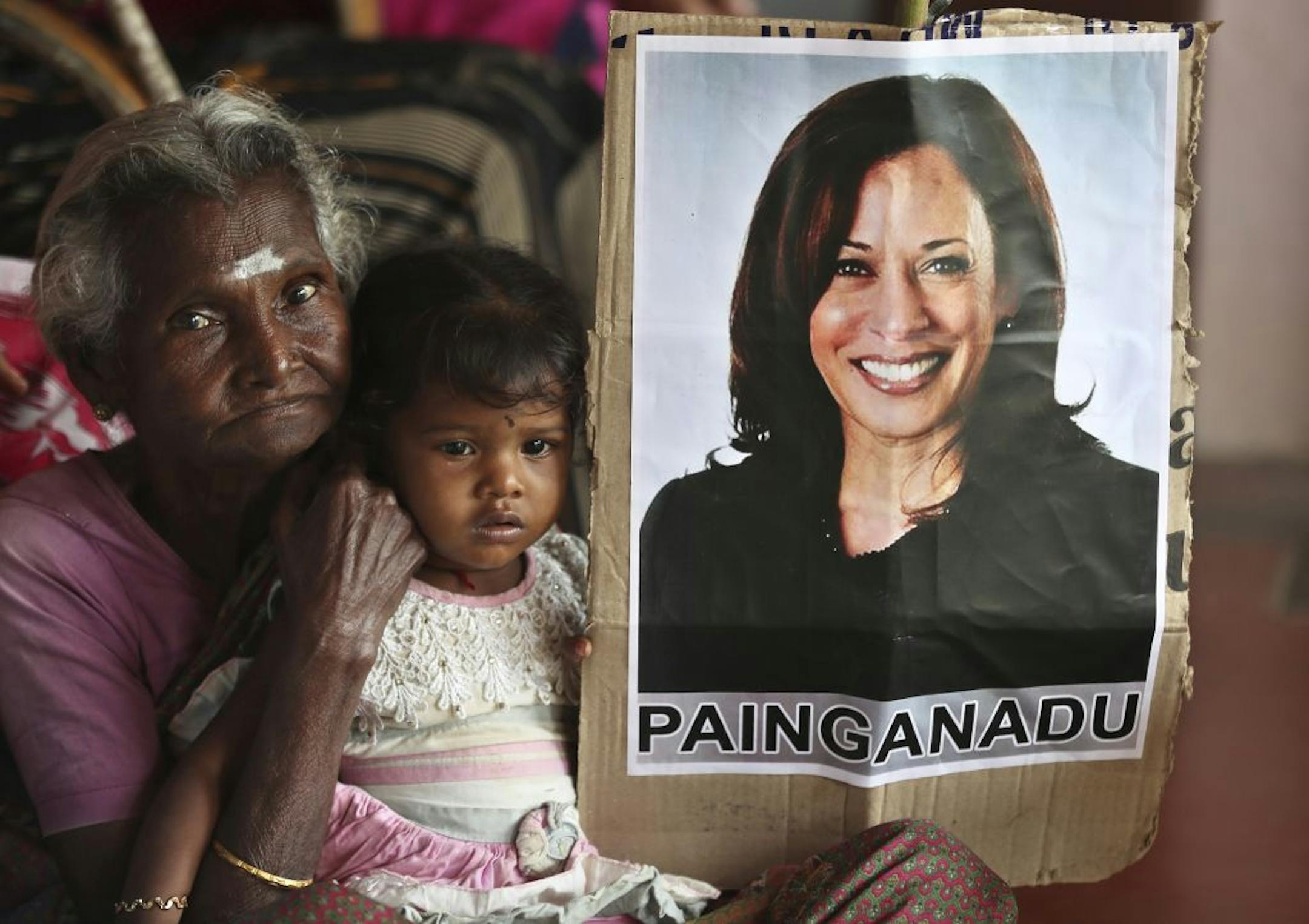 An Indian girl sits in the lap of an elderly woman next to a placard featuring U.S. democratic vice presidential candidate Sen. Kamala Harris at the ancestral house of the Vandayar family, where celebrations are planned should the Democratic Party win the presidential elections, in Painganadu a neighboring village of Thulasendrapuram, south of Chennai, Tamil Nadu state, India, Friday, Nov. 6, 2020. The lush green village of Thulasendrapuram is the hometown of Harris' maternal grandfather who mig