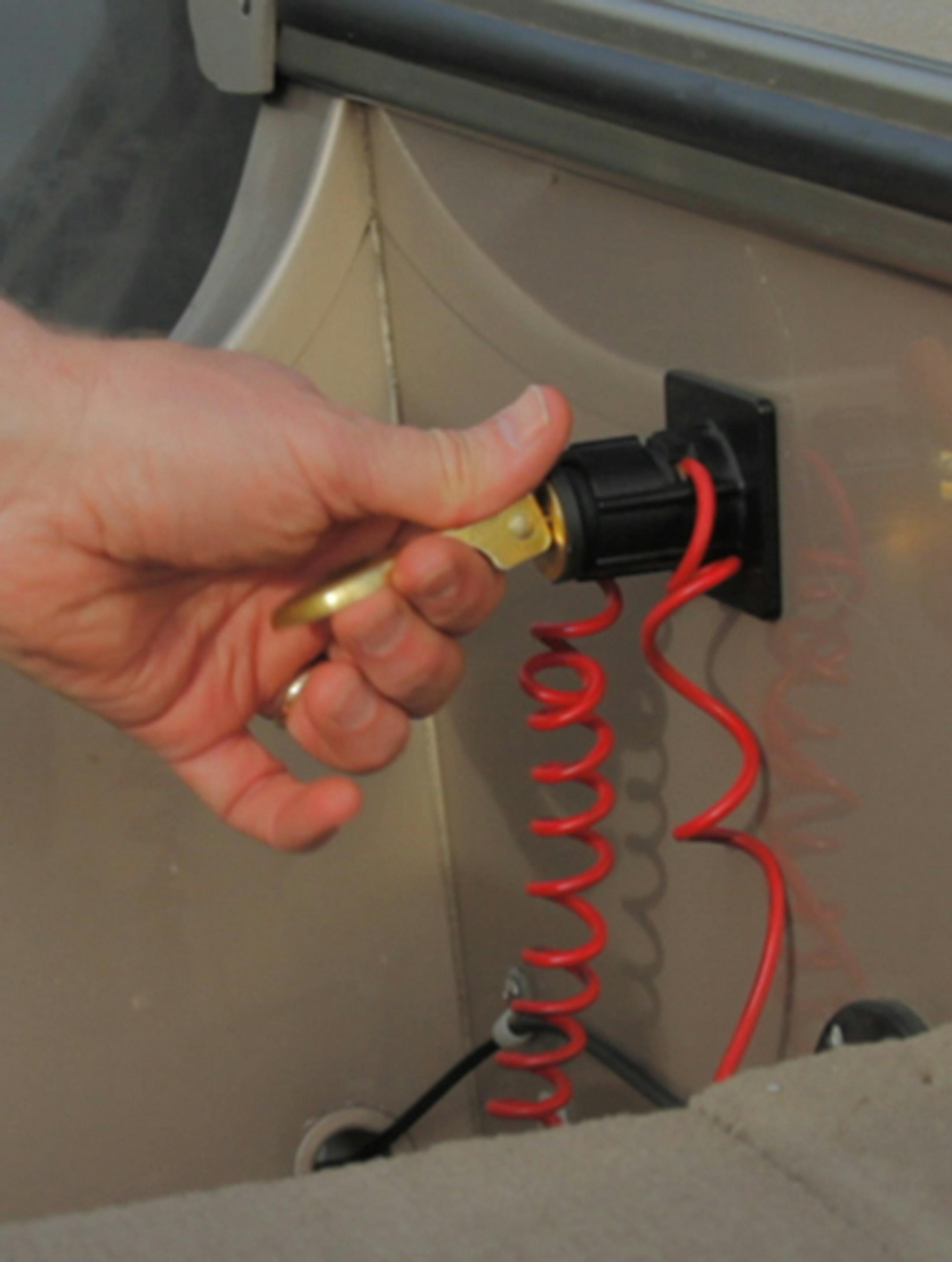 The black plastic Plug Dock device is shown holding a brass boat plug and orange kill-switch tether. The boater can't start the engine until the kill-switch tether is connected near the engine. Photo courtsey Jon Harkness