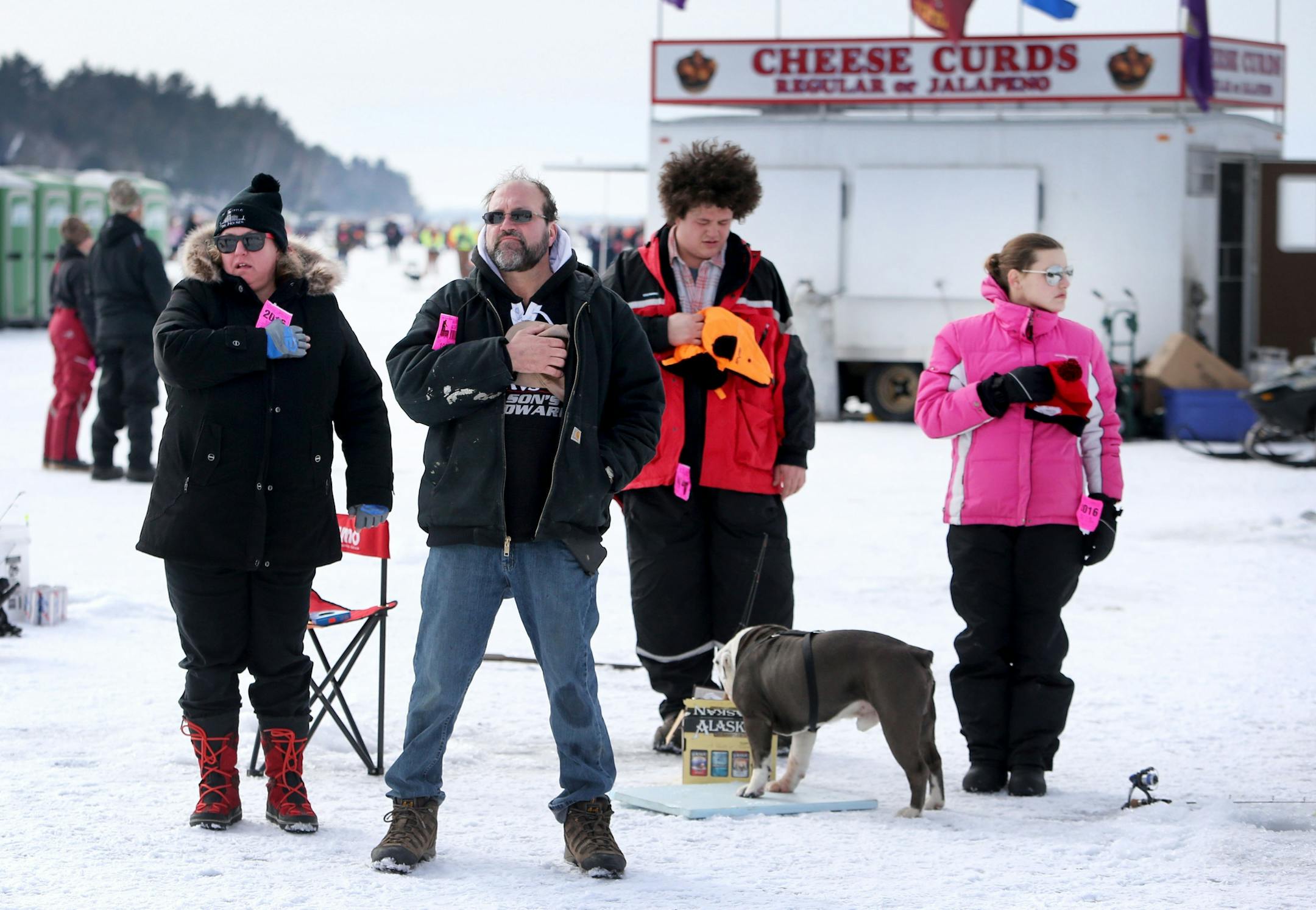 Members of the Olson family of Montevideo with their dog Gravy, an English bulldog, place their hands over their hearts during the playing of the National Anthem on Hole in the Day Bay of Gull Lake during the Ice Fishing Extravaganza Saturday, Feb. 6, 2016, in Brainerd, MN.