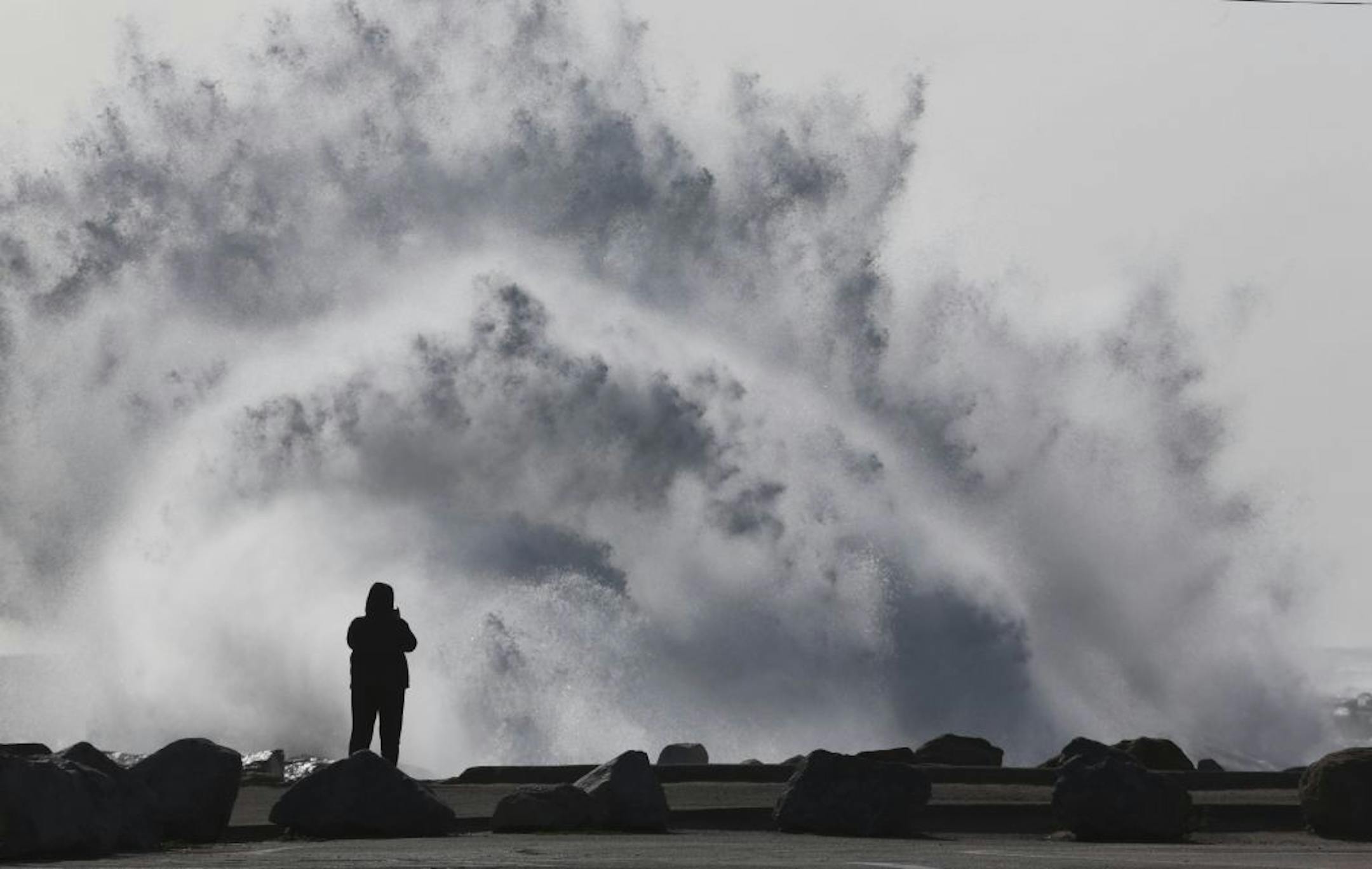 A person stands at the breakwall as waves crash at Cabrillo Beach in San Pedro, Calif. High winds rolled through Los Angeles Monday morning causing large surf.